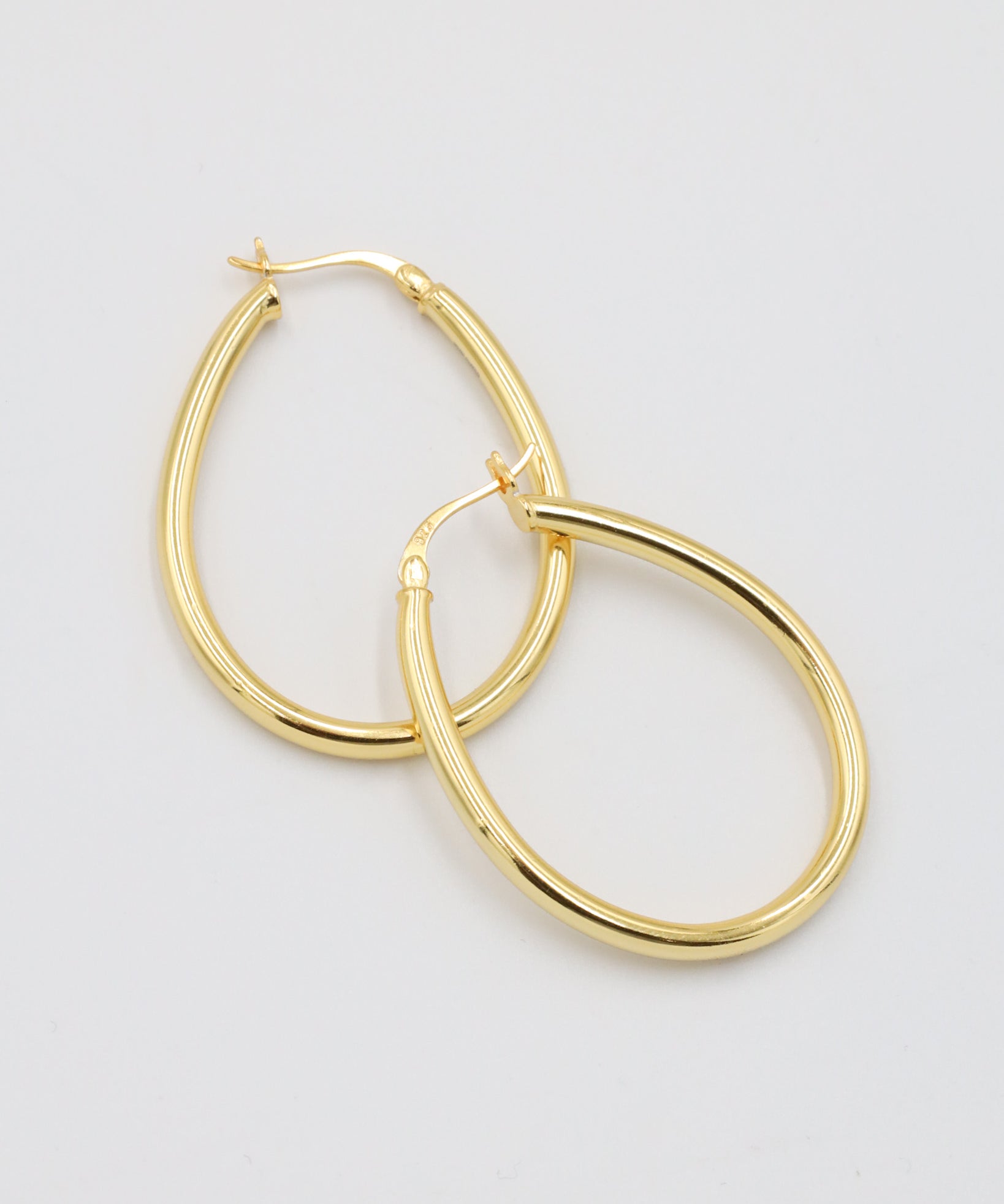 A pair of gold creole earrings with a latch back clasp on a white background.