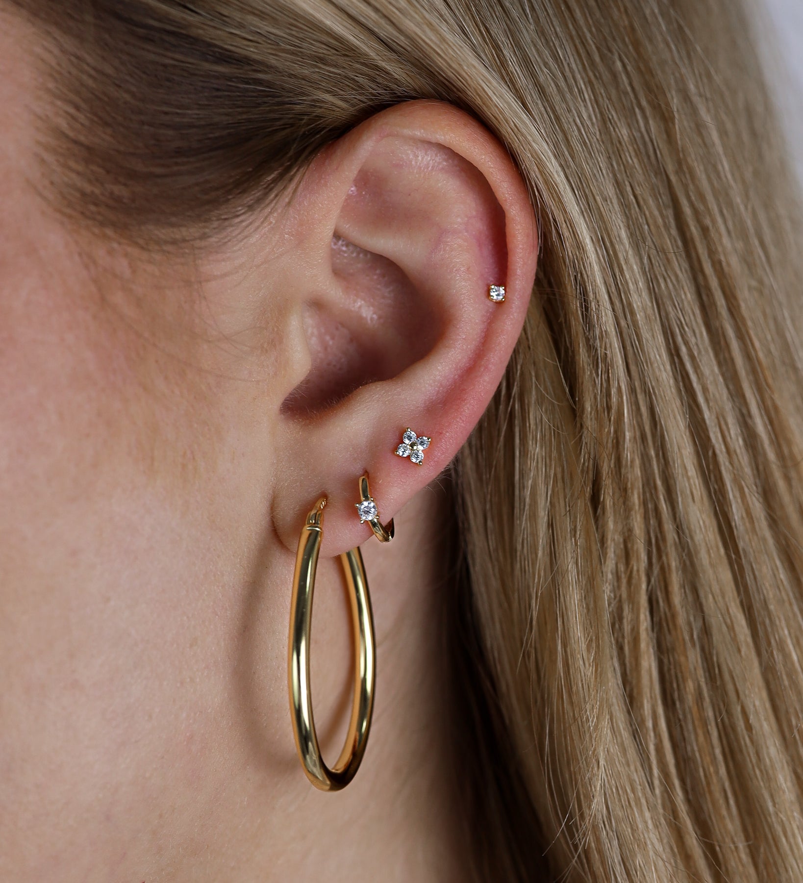 Close-up of an ear wearing gold hoop earrings with small diamond stud earrings.