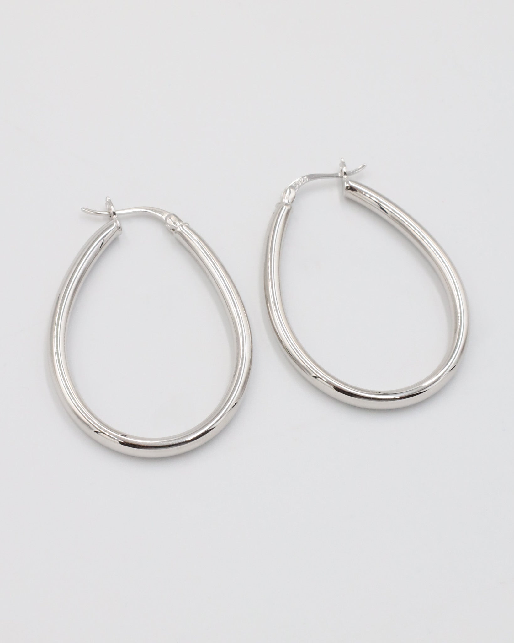 A pair of silver creole earrings with a latch back clasp on a white background.