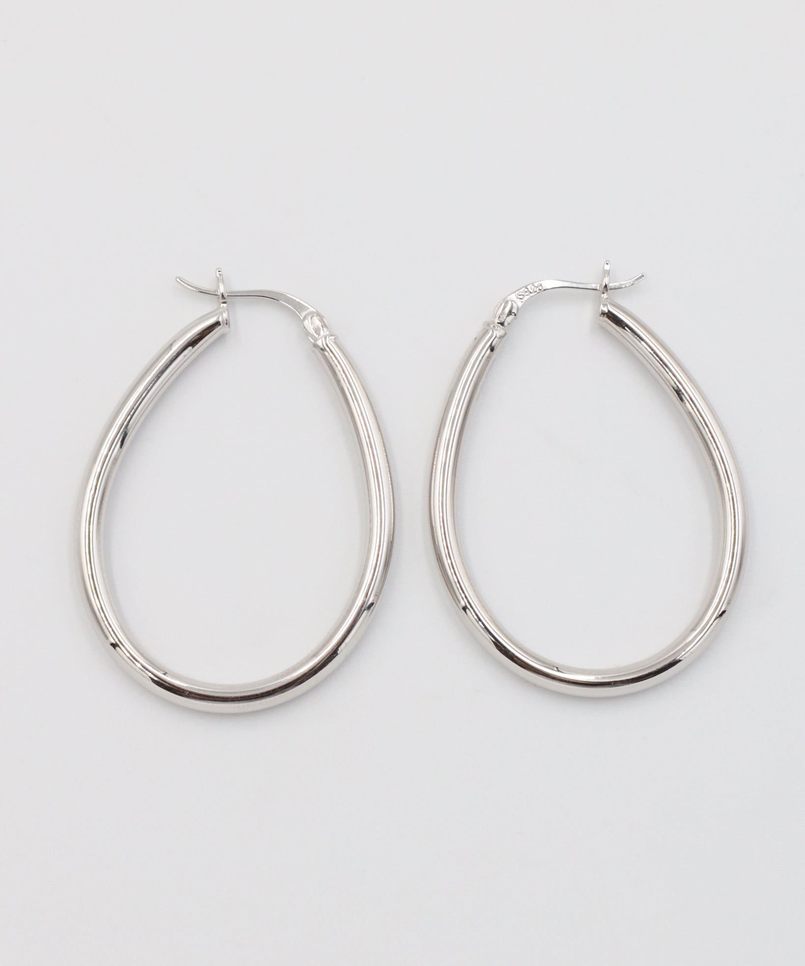 A pair of silver creole earrings with a latch back clasp on a white background.