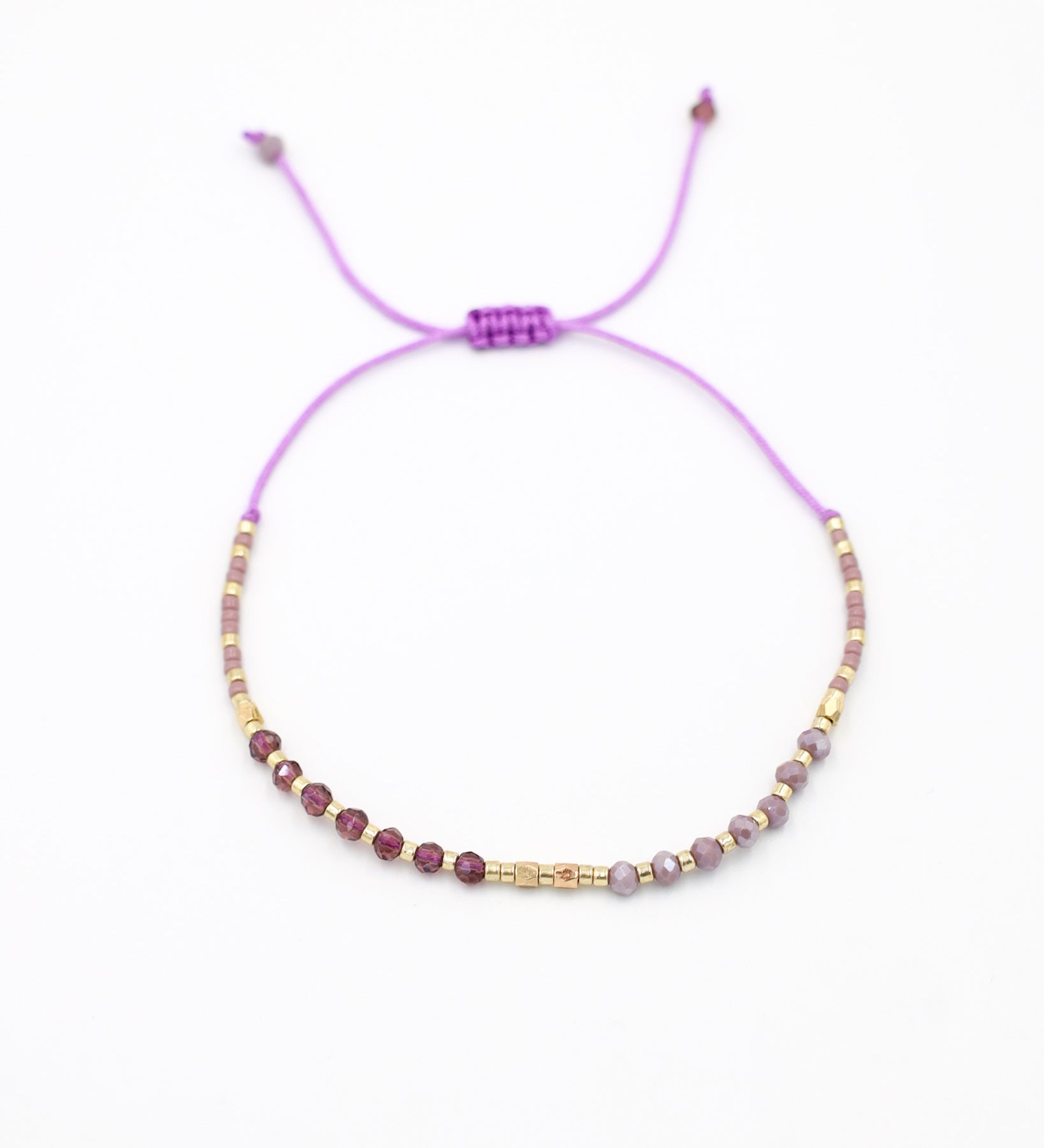 An adjustable gold-colored bracelet with a series of round beads and rhinestone accents, featuring a purple clasp.