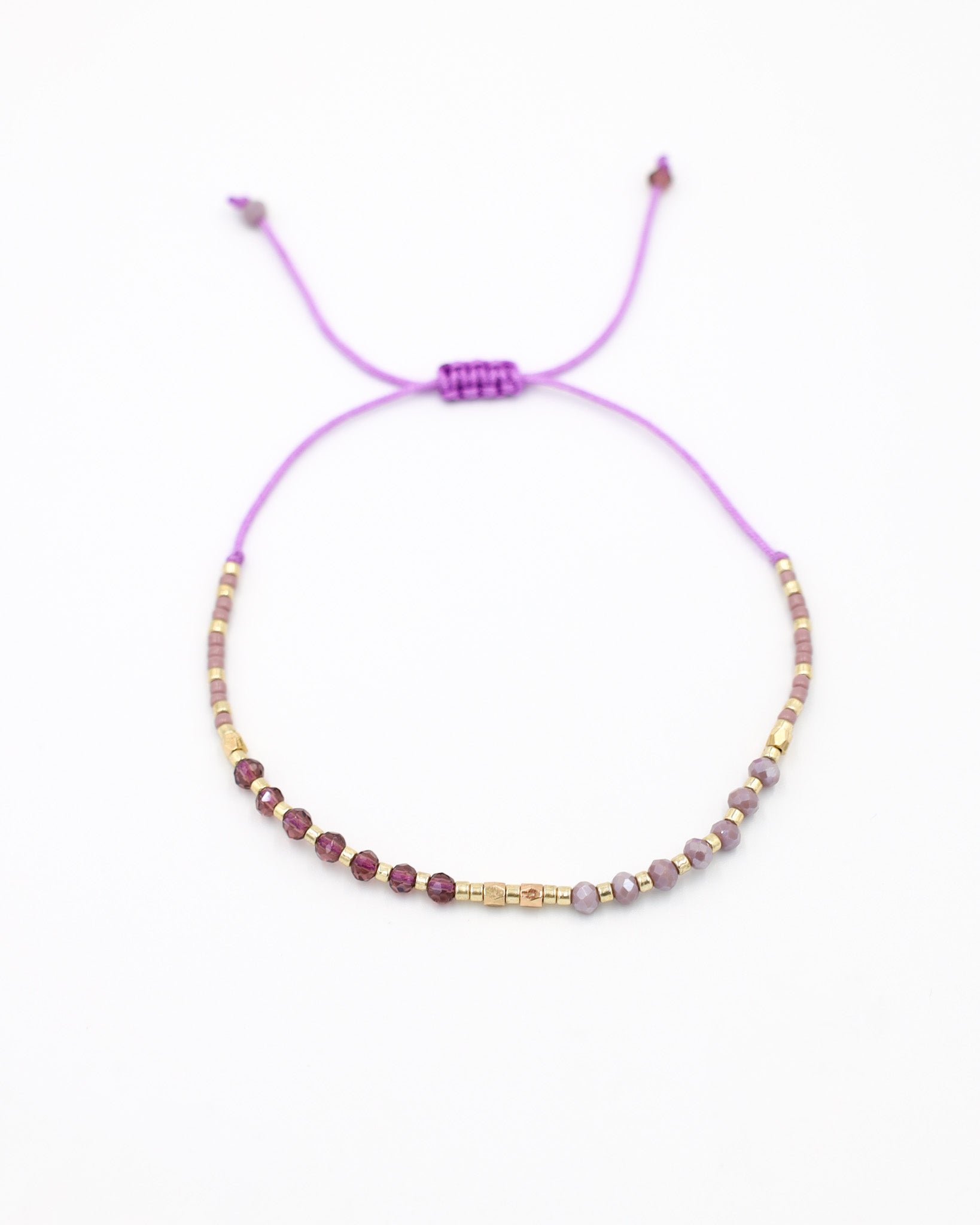 An adjustable gold-colored bracelet with a series of round beads and rhinestone accents, featuring a purple clasp.
