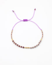 An adjustable gold-colored bracelet with a series of round beads and rhinestone accents, featuring a purple clasp.