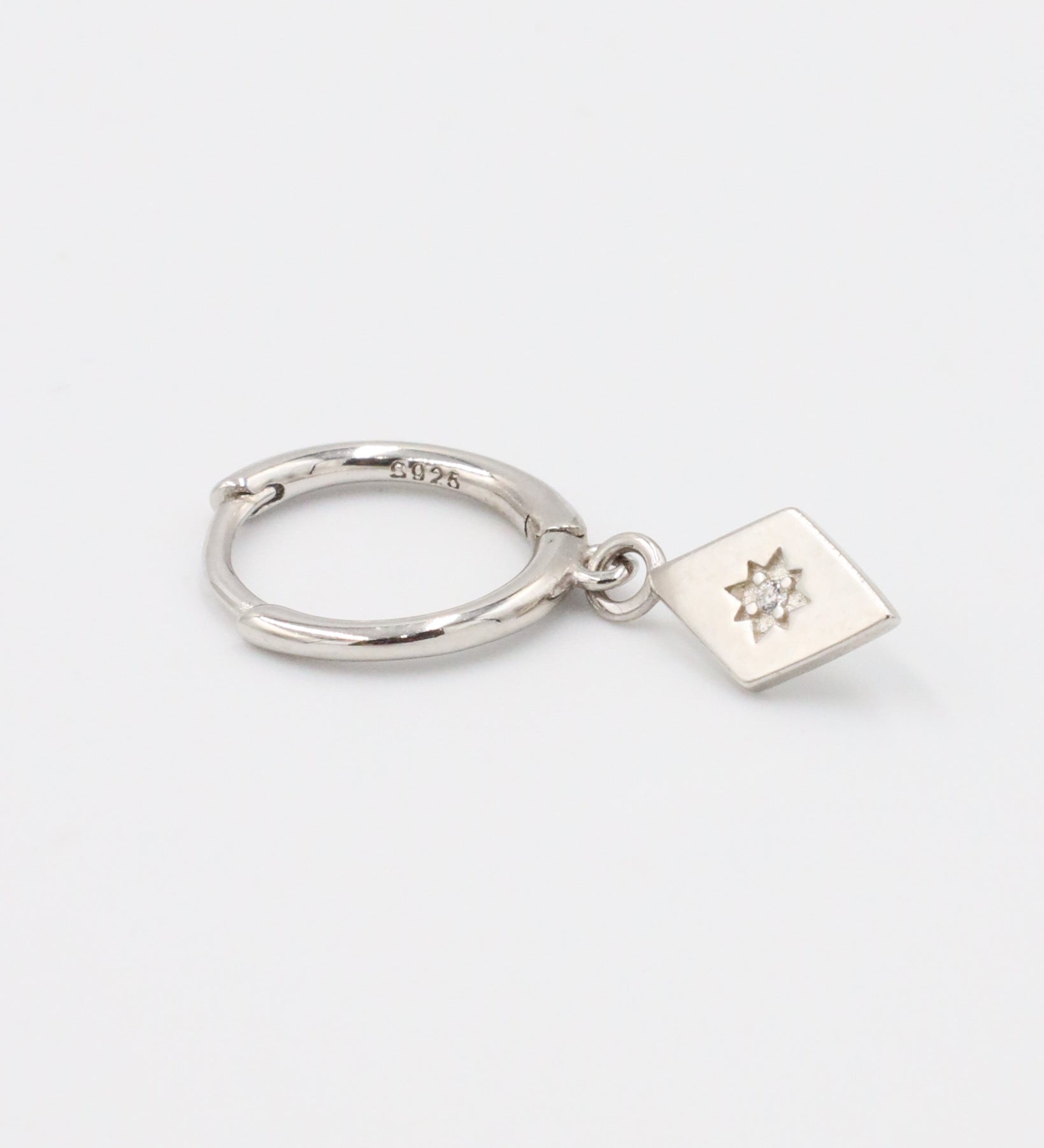 A single Patricia Silver earring, showcasing a diamond-shaped pendant with a star engraving and cubic zirconia stone, attached to a sleek sterling silver hoop.