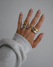 A gold-colored ring with multiple gemstones set around its circumference worn on a hand. 