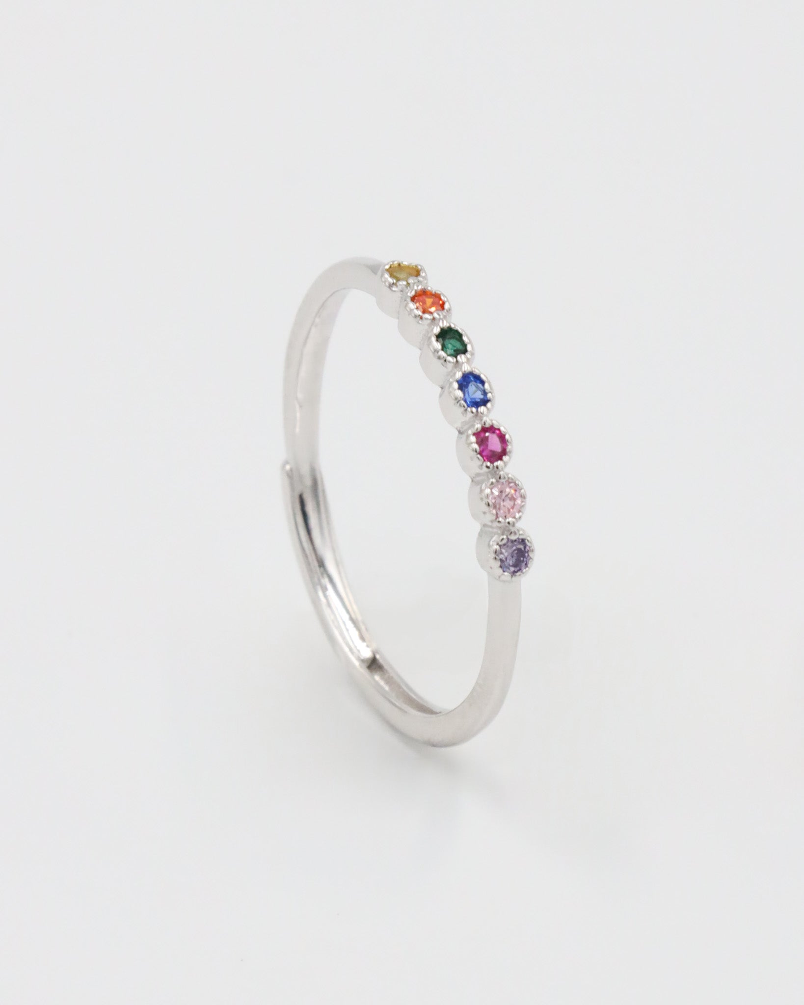 A silver ring with multiple colorful gemstones set in a line on a white background.