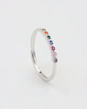A silver ring with multiple colorful gemstones set in a line on a white background.