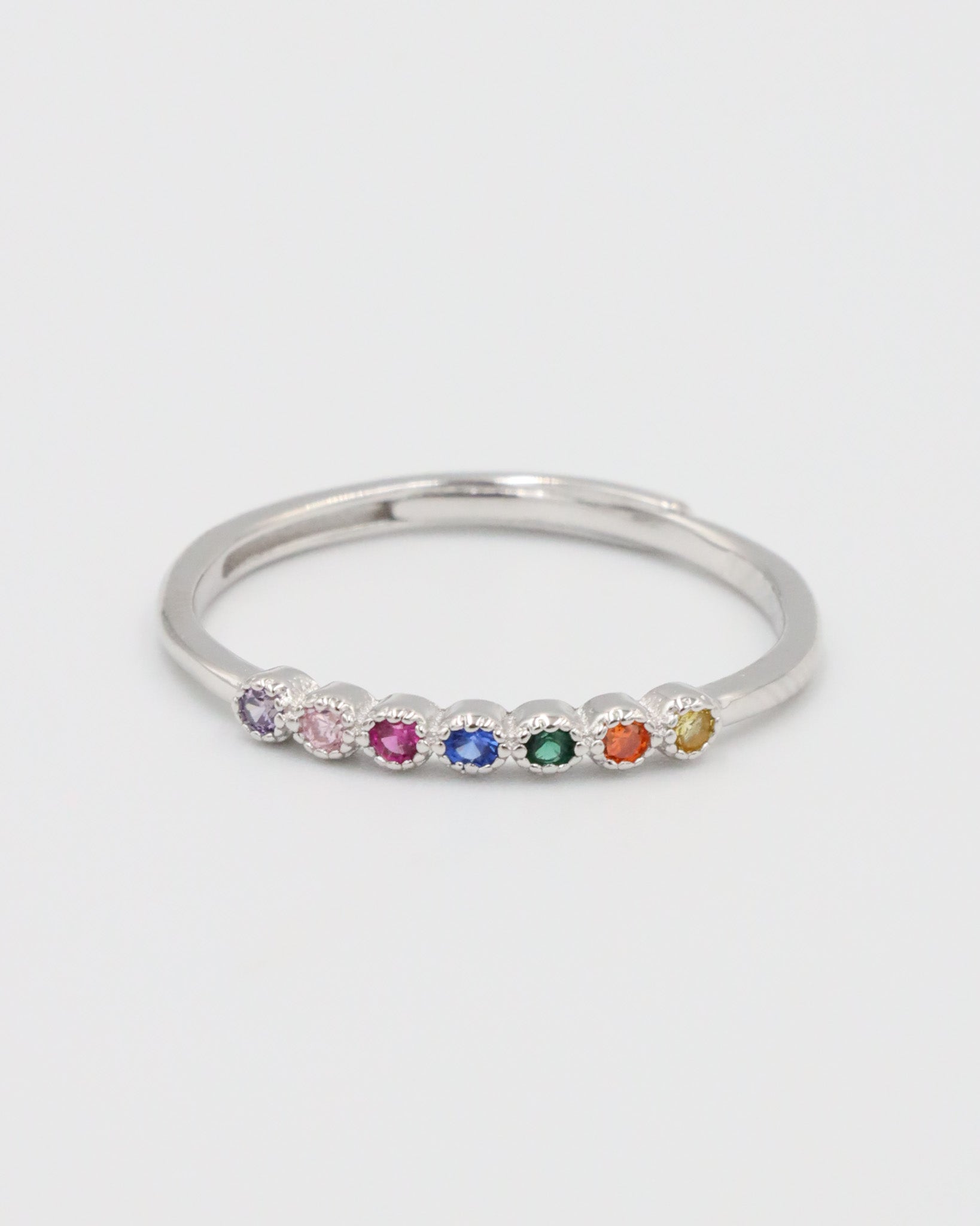 A silver ring with multiple colorful gemstones set in a line on a white background.