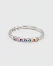 A silver ring with multiple colorful gemstones set in a line on a white background.