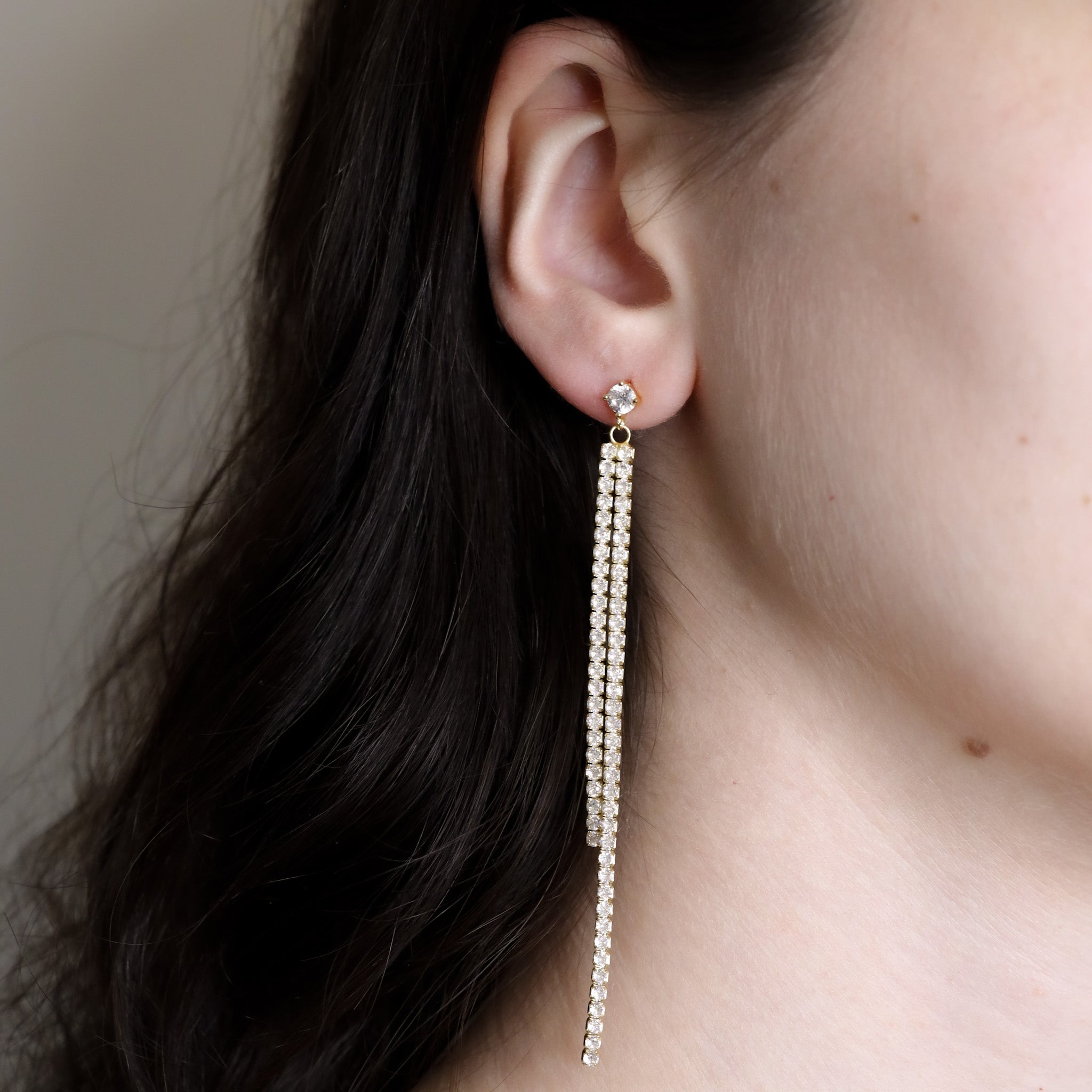A gold-colored stud earrings with small crystal embellishments worn by a person.
