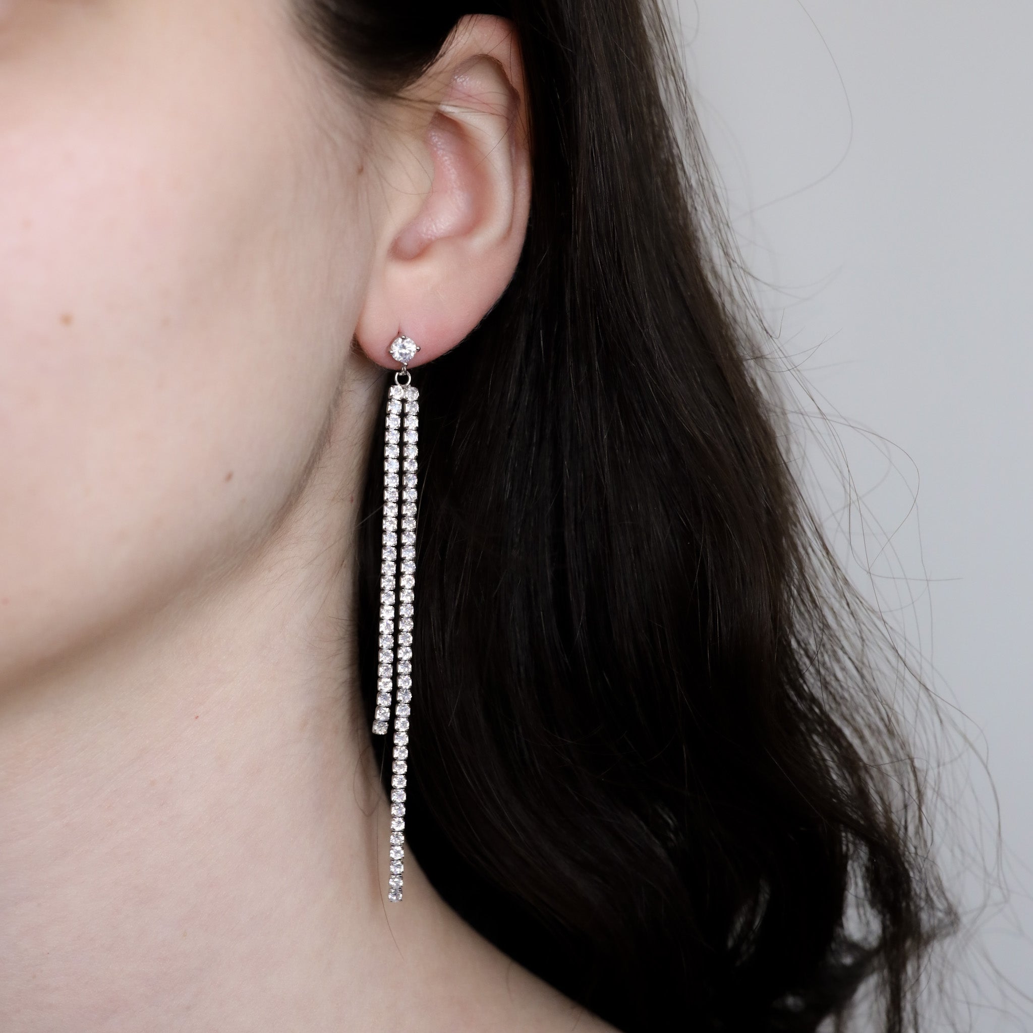Silver earrings with dangling crystal embellishments worn by a person.