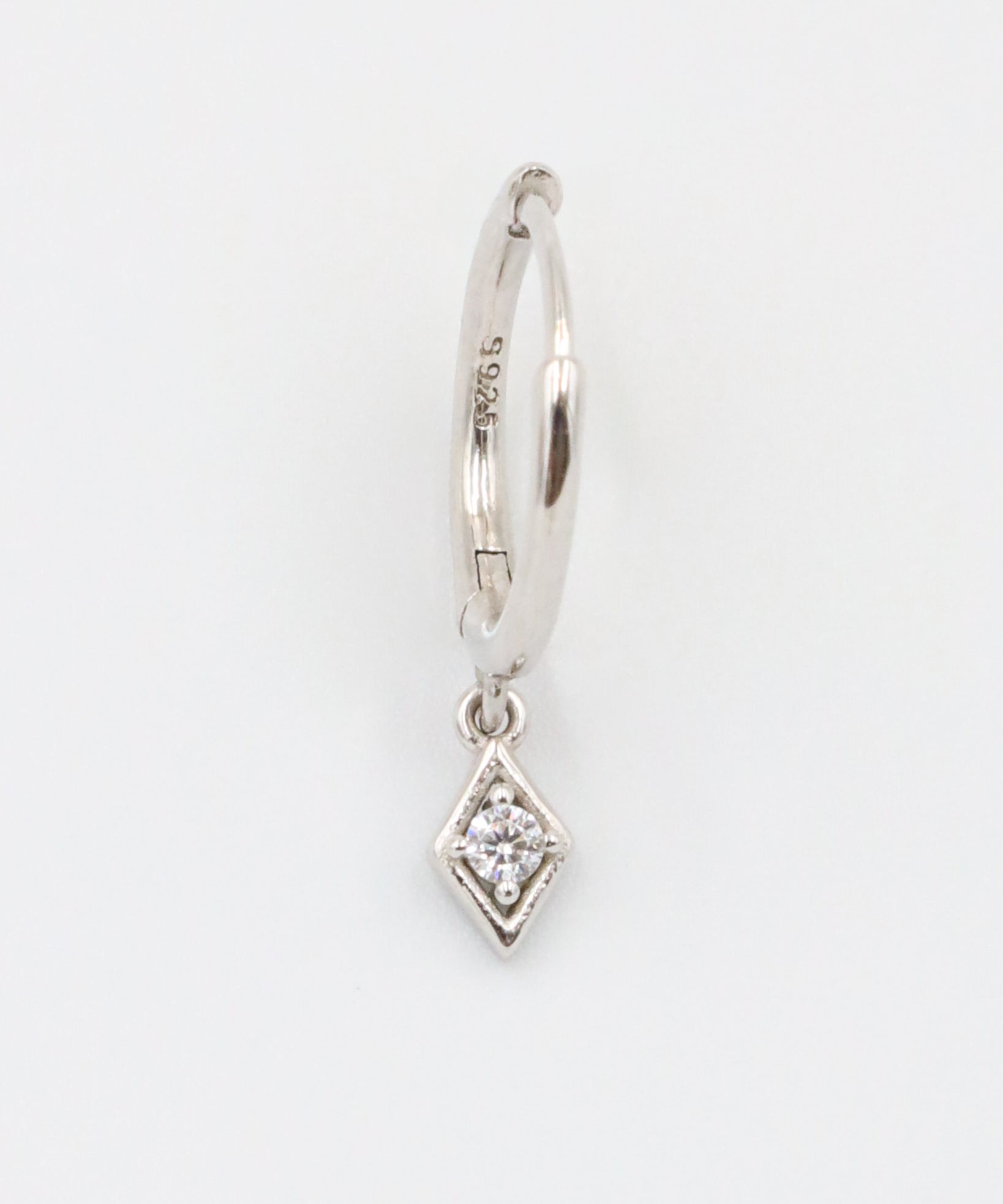 A single silver hoop earring with a small diamond-shaped pendant attached to it, displayed against a white background.