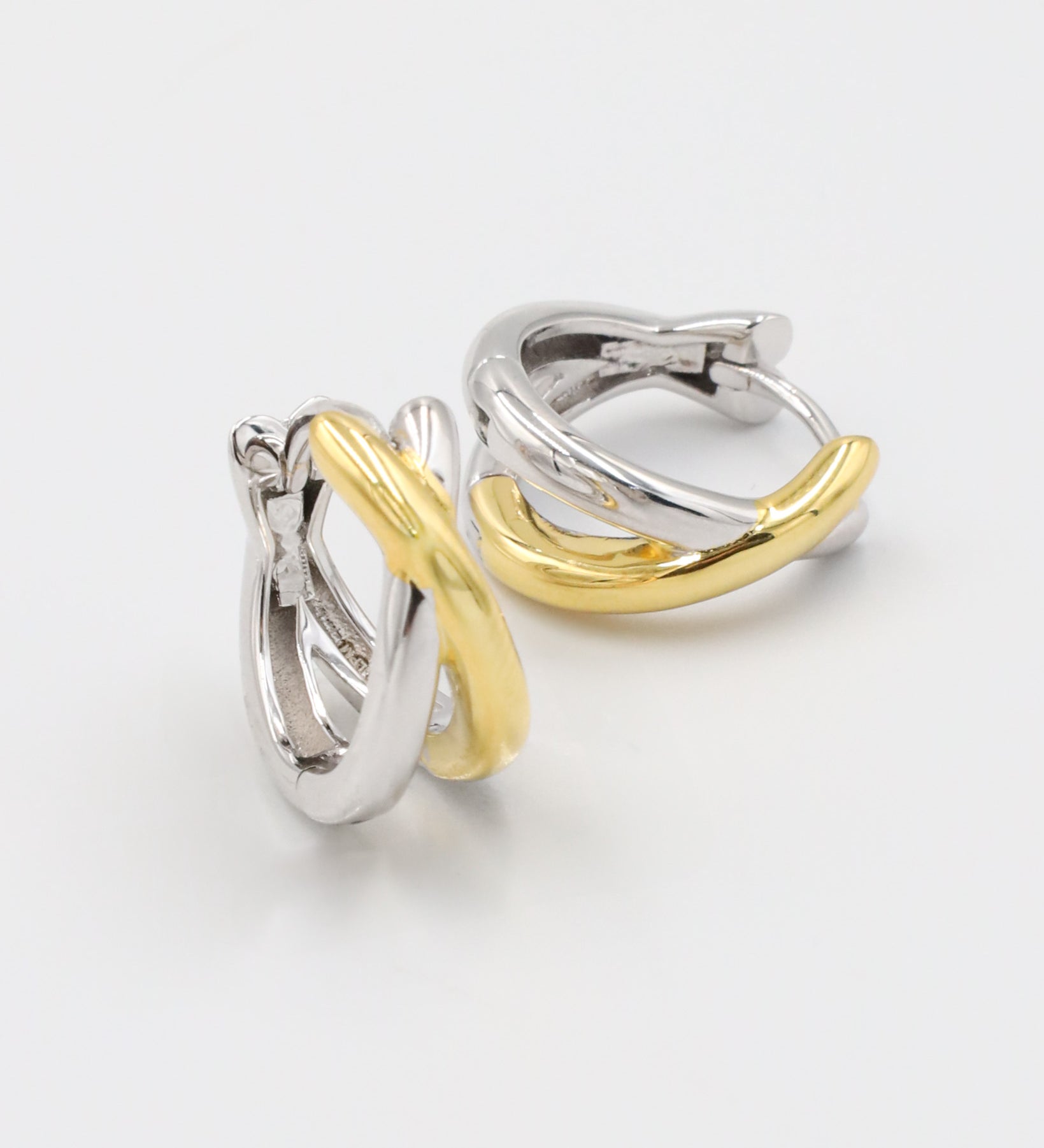 A pair of hoop earrings with one half in silver and the other half in gold color, connected by a hinged clasp.