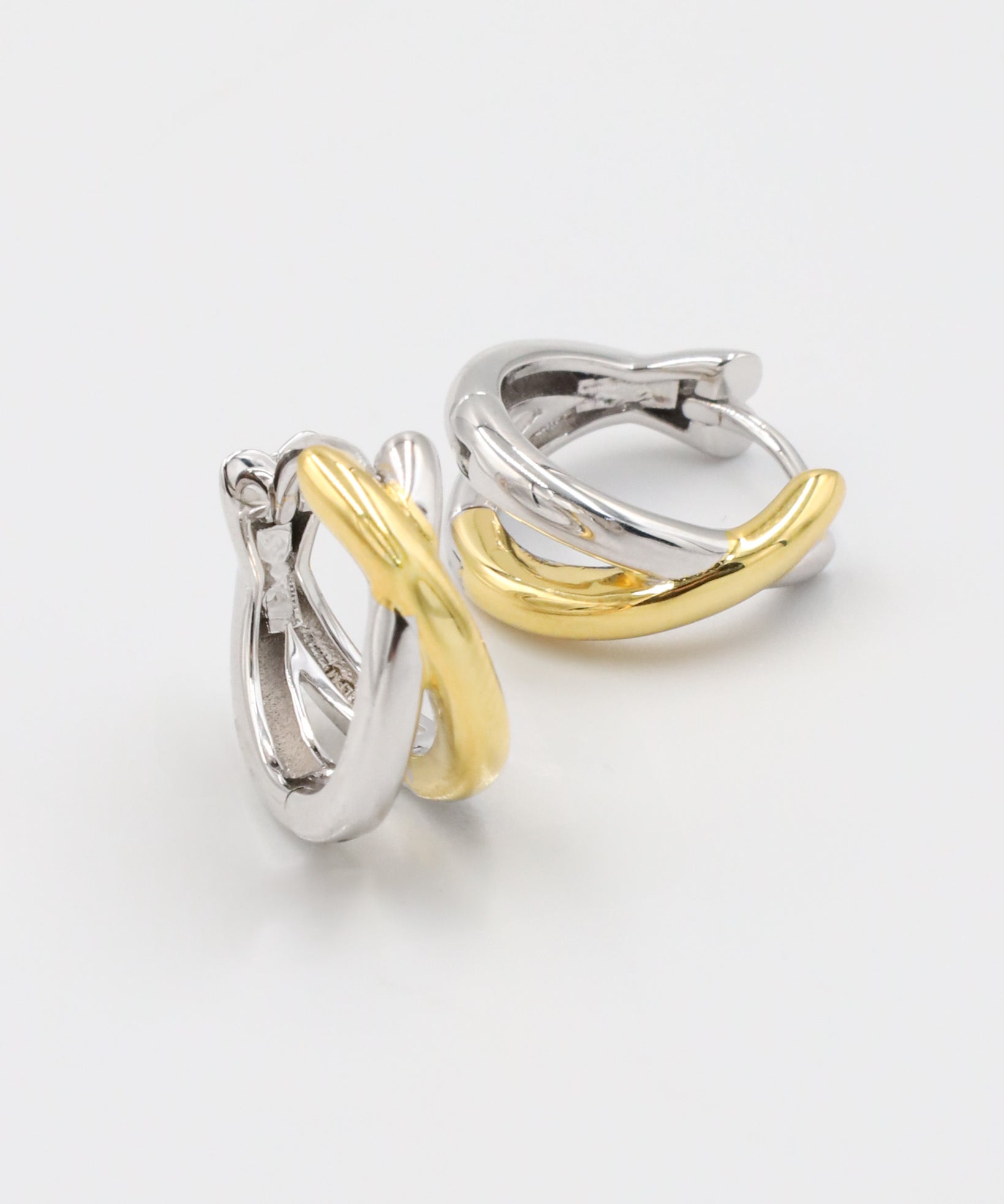 A pair of hoop earrings with one half in silver and the other half in gold color, connected by a hinged clasp.