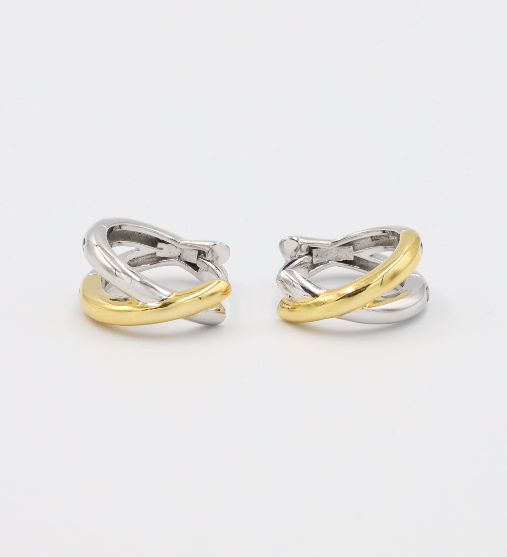 A pair of bicolor hoop earrings with a hinged clasp, featuring mixed metals design, predominantly silver with gold accents.