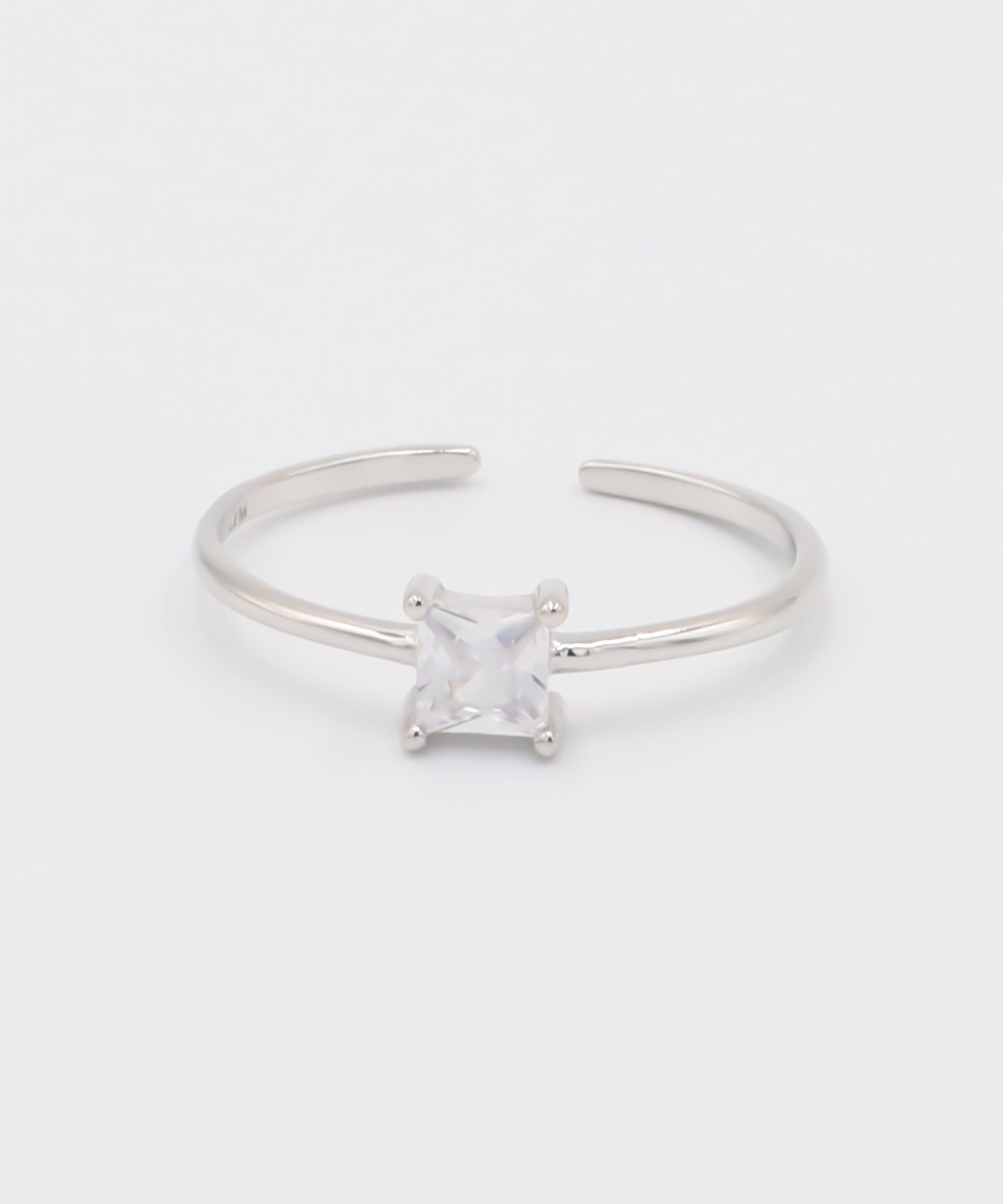 A silver ring with a clear, square-cut central gemstone, surrounded by smaller clear gemstones set in a recycled 925 sterling silver band, with a textured white background.