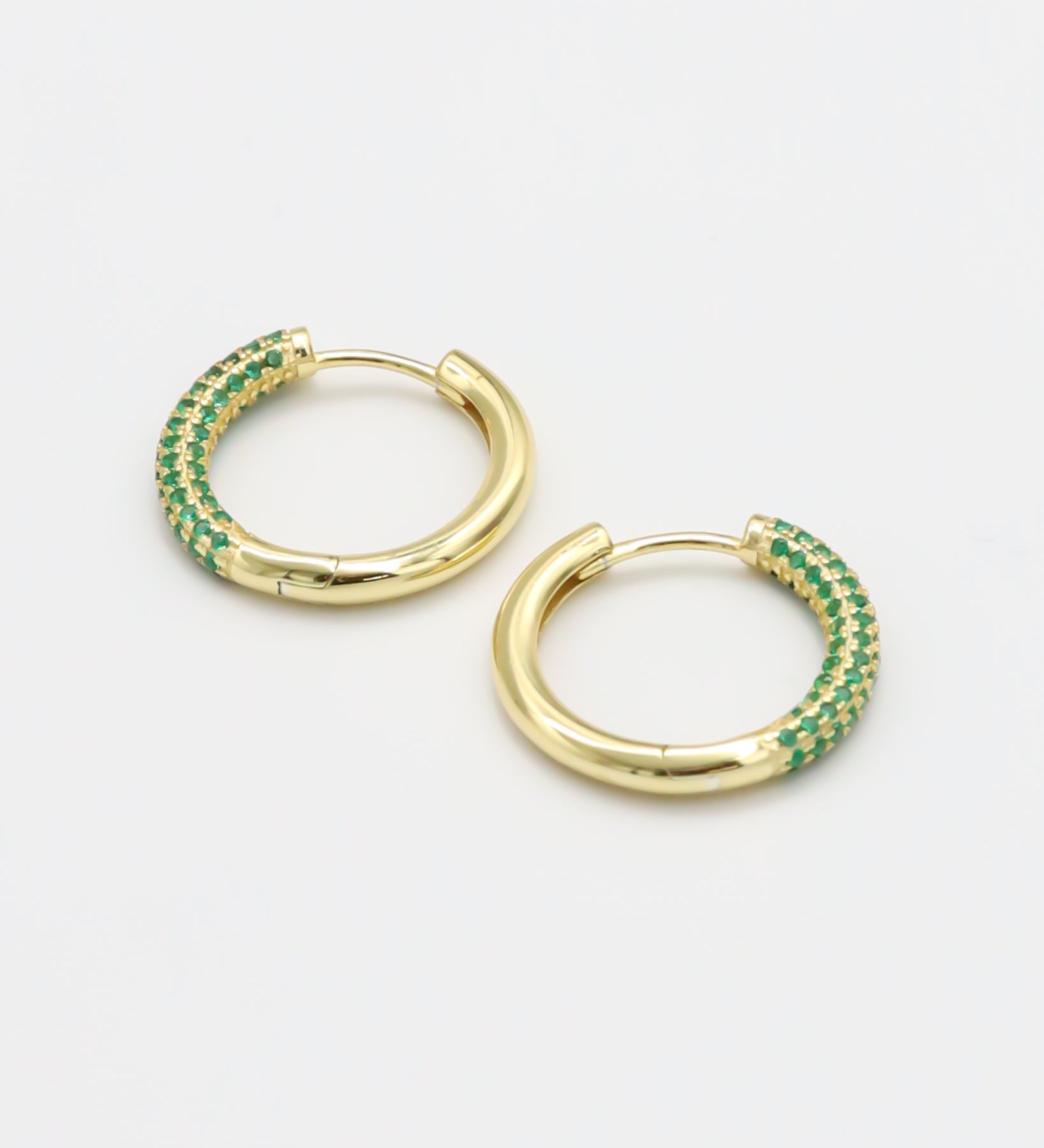 A pair of gold-colored hoop earrings with green accents, displayed against a white background.
