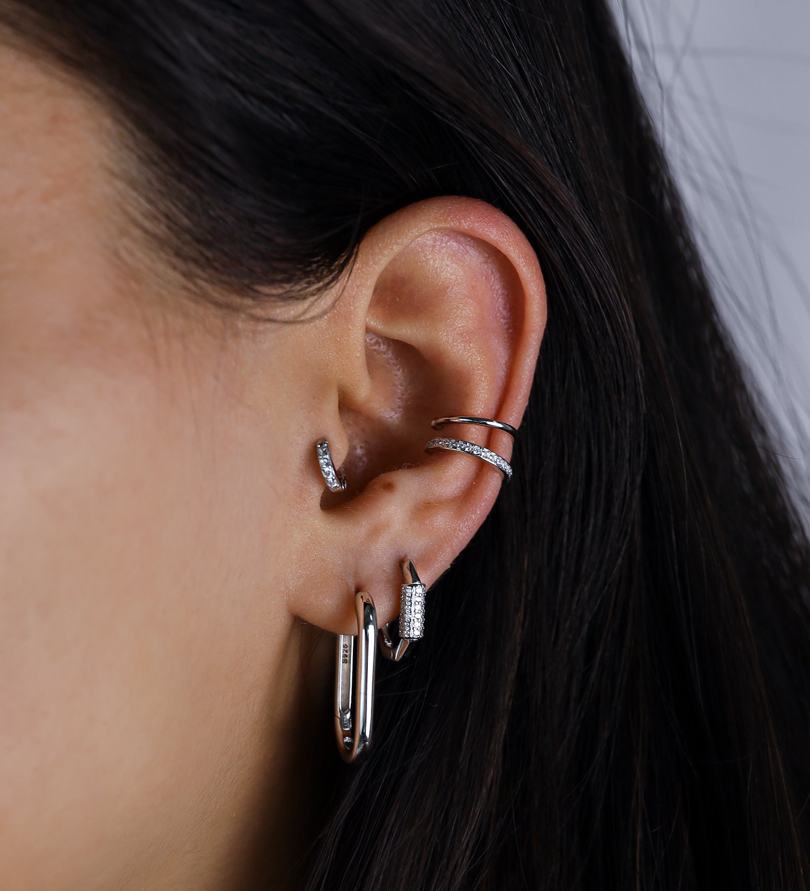 Close-up of an ear with multiple silver earrings against a neutral background