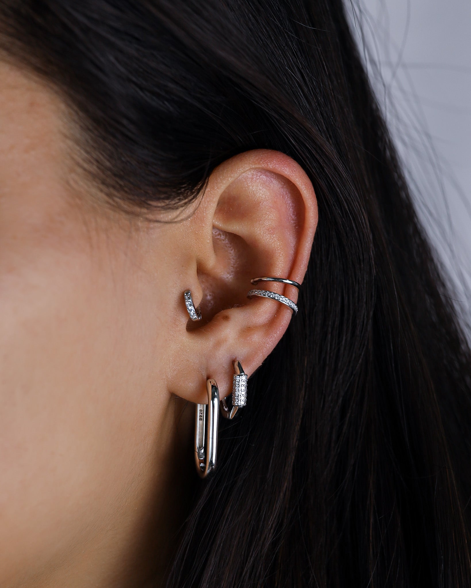 Close-up of an ear with multiple silver earrings against a neutral background