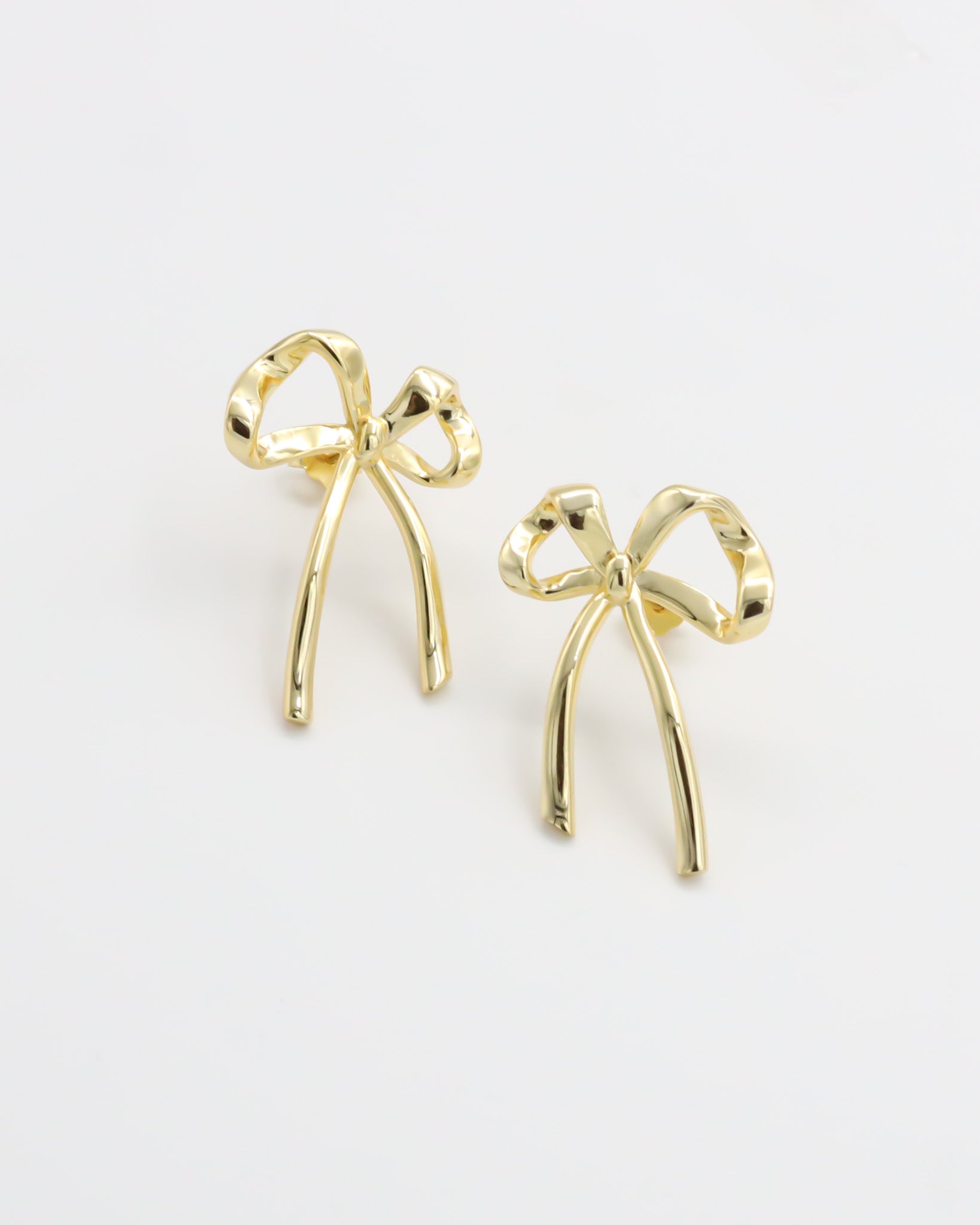 A pair of gold-colored ribbon-shaped stud earrings on a white background