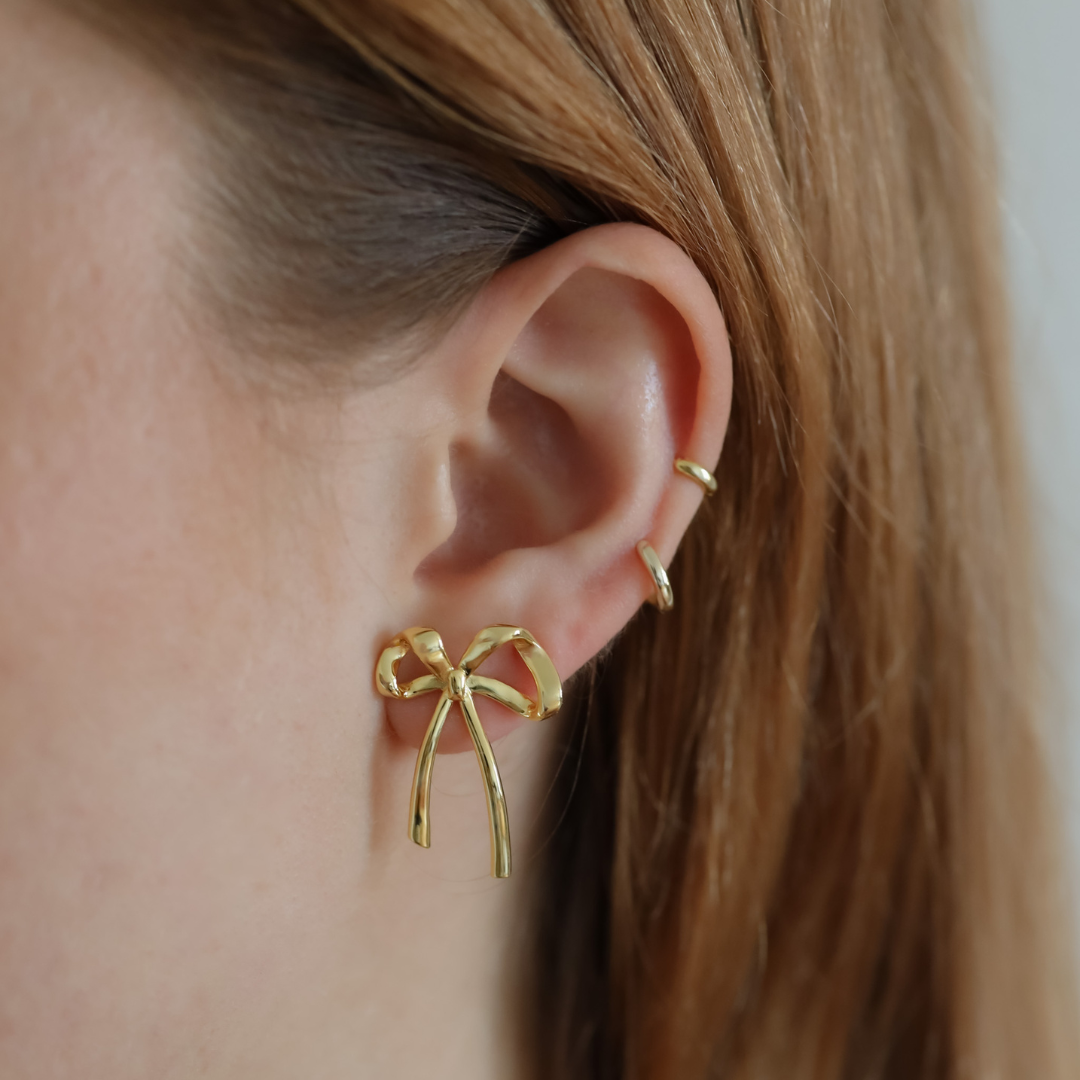 Close-up of a person wearing the Ribbon earring in gold on the lobe combined with Lu hoops on the helix.