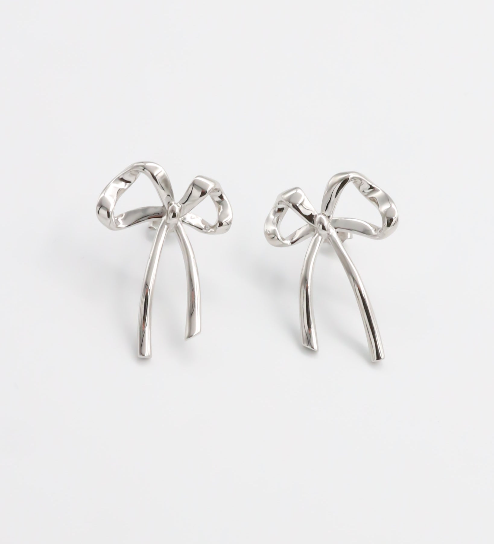 A pair of silver bow-shaped earrings on a white background
