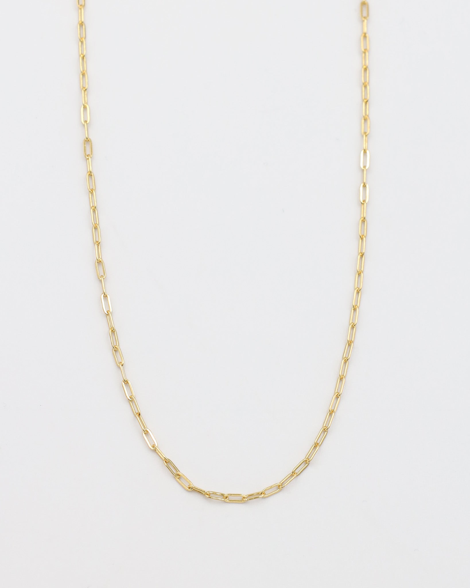 A gold-colored necklace with a chain link design, laid out on a plain background.