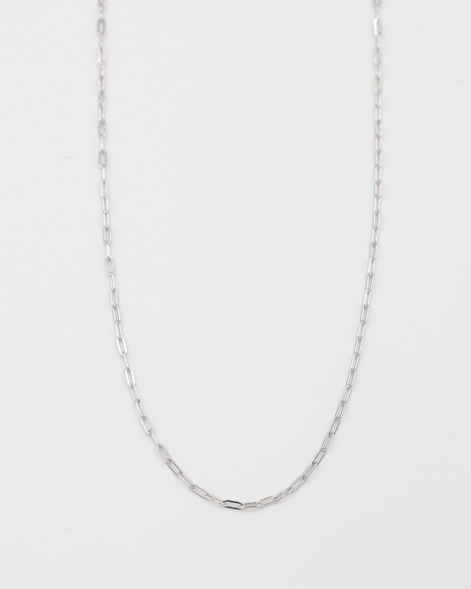 A silver necklace with a chain link design, laid out on a plain background.