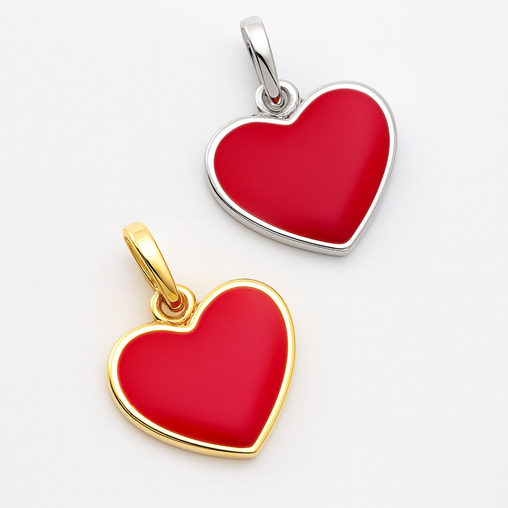 Two heart-shaped pendants, one gold and one silver, on a light gray background.