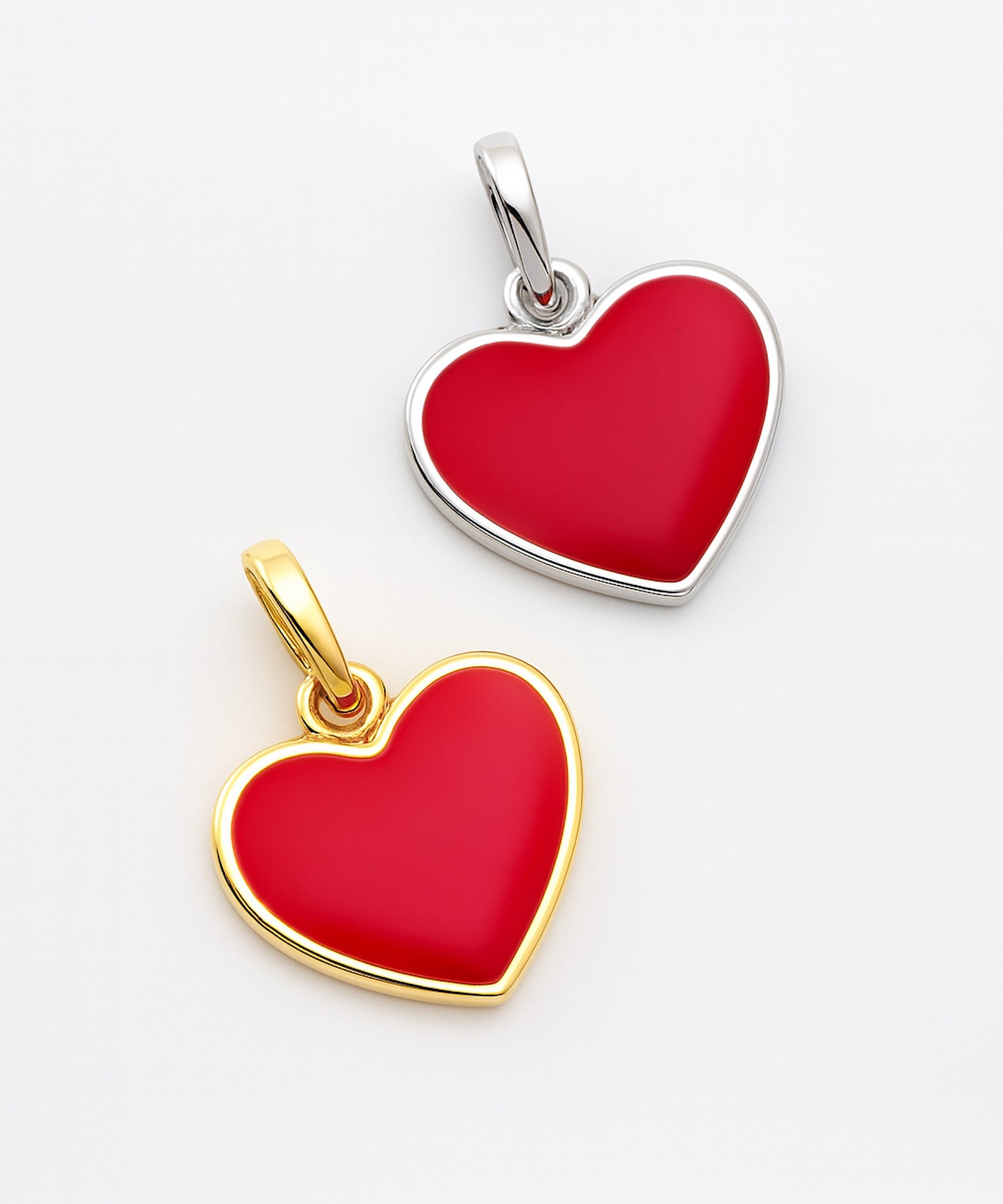 Two heart-shaped pendants, one gold and one silver, on a light gray background.