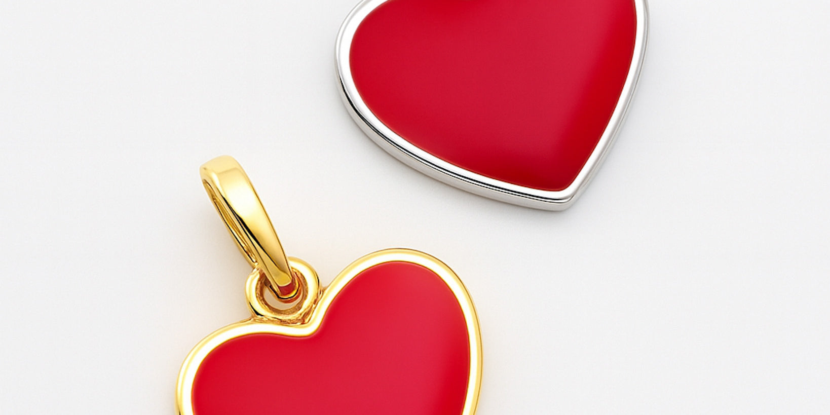 Two heart-shaped pendants, one gold and one silver, on a light gray background.