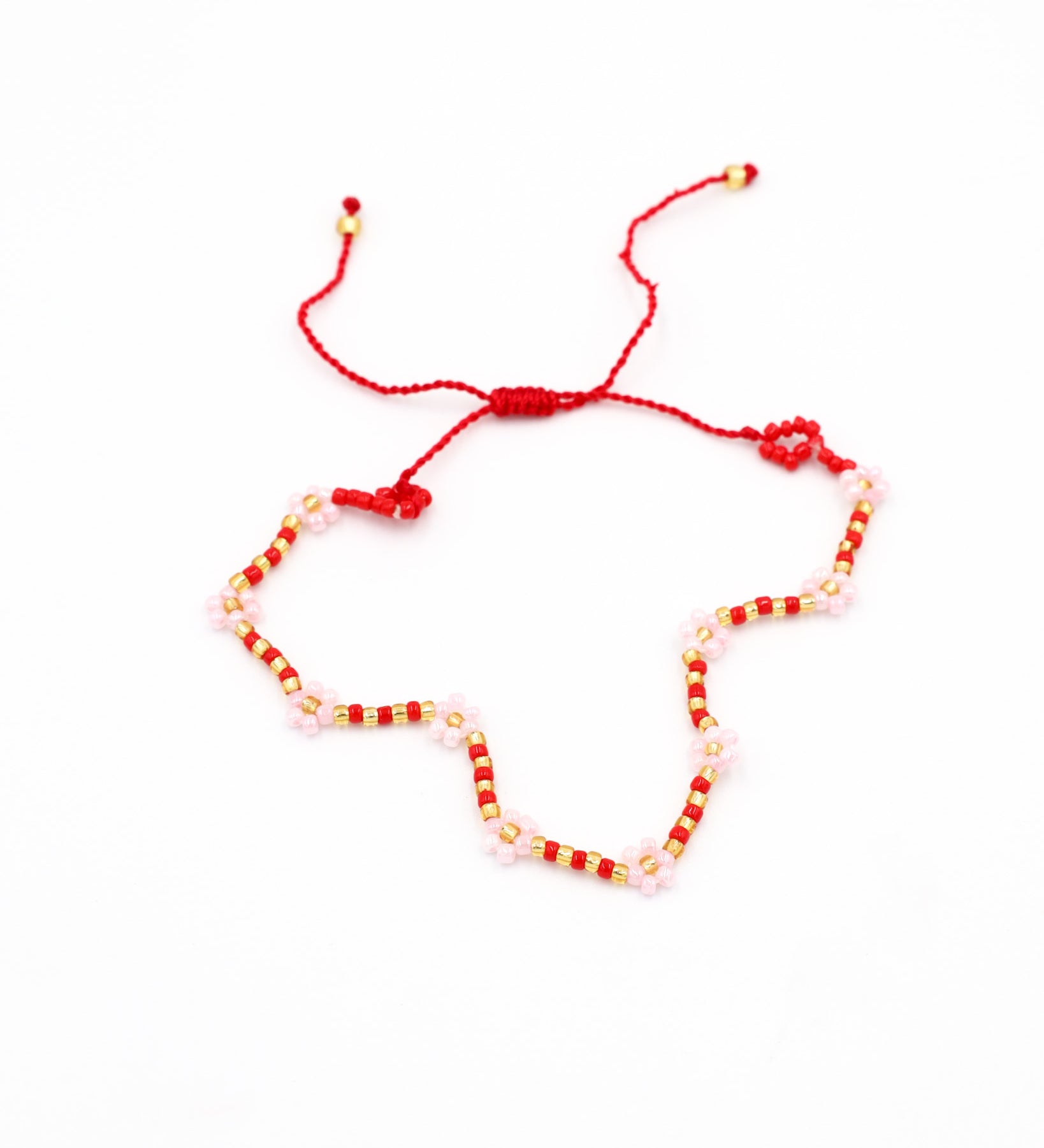 Beaded bracelet in red, pink, and gold tones with a zigzag pattern and adjustable sliding closure, laid flat on a white background.