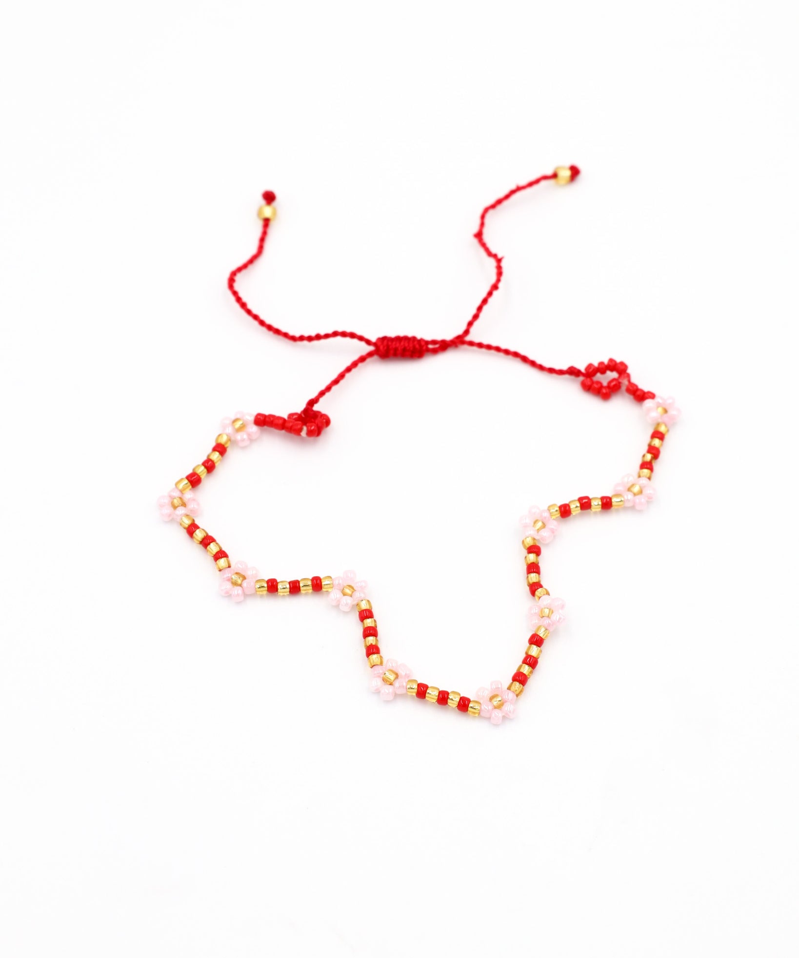 Beaded bracelet in red, pink, and gold tones with a zigzag pattern and adjustable sliding closure, laid flat on a white background.