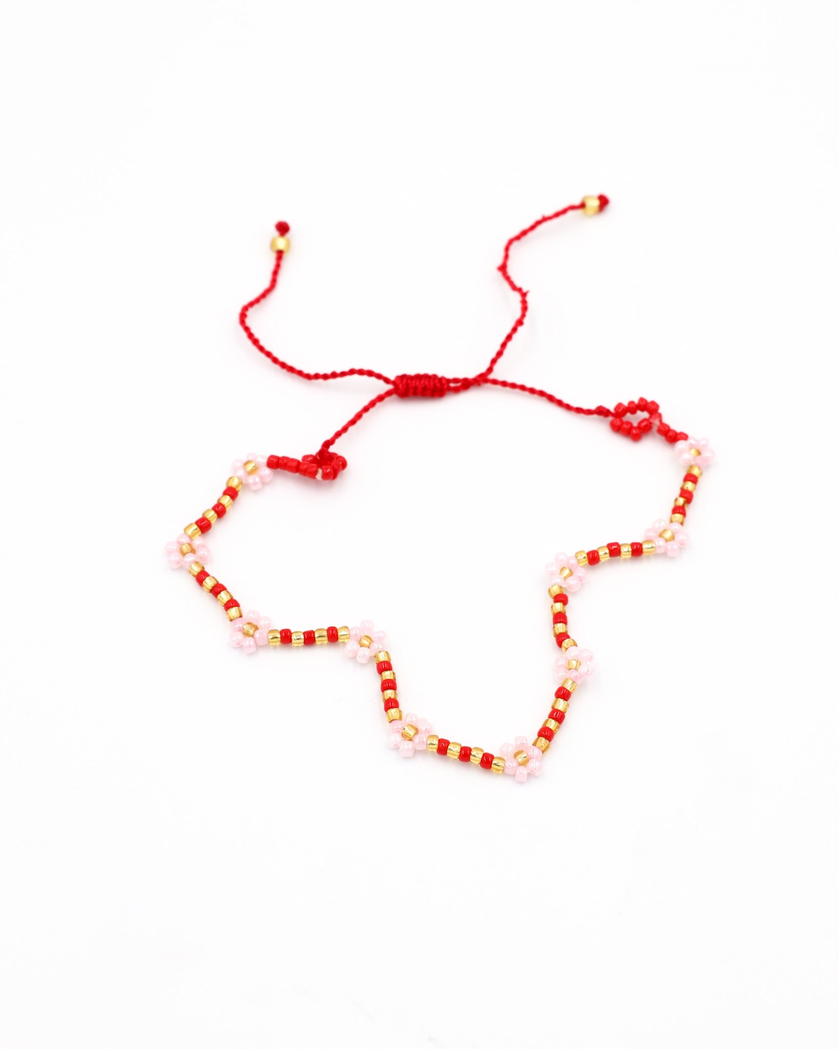 Beaded bracelet in red, pink, and gold tones with a zigzag pattern and adjustable sliding closure, laid flat on a white background.