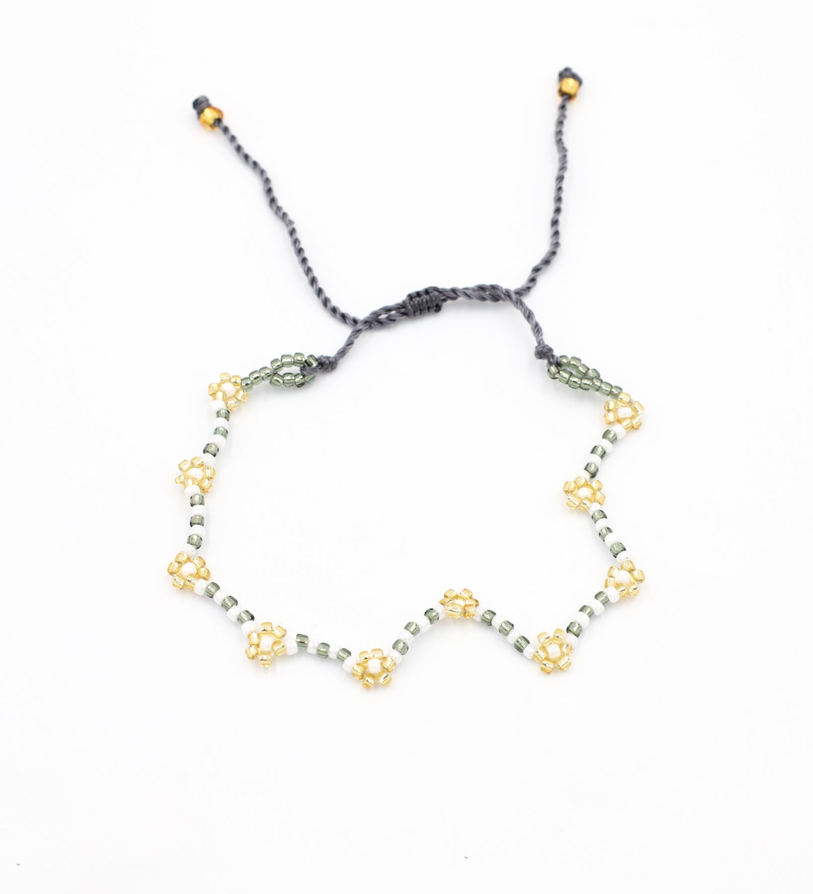 Beaded bracelet in gray, white and gold tones with a zigzag pattern and adjustable sliding closure, laid flat on a white background.