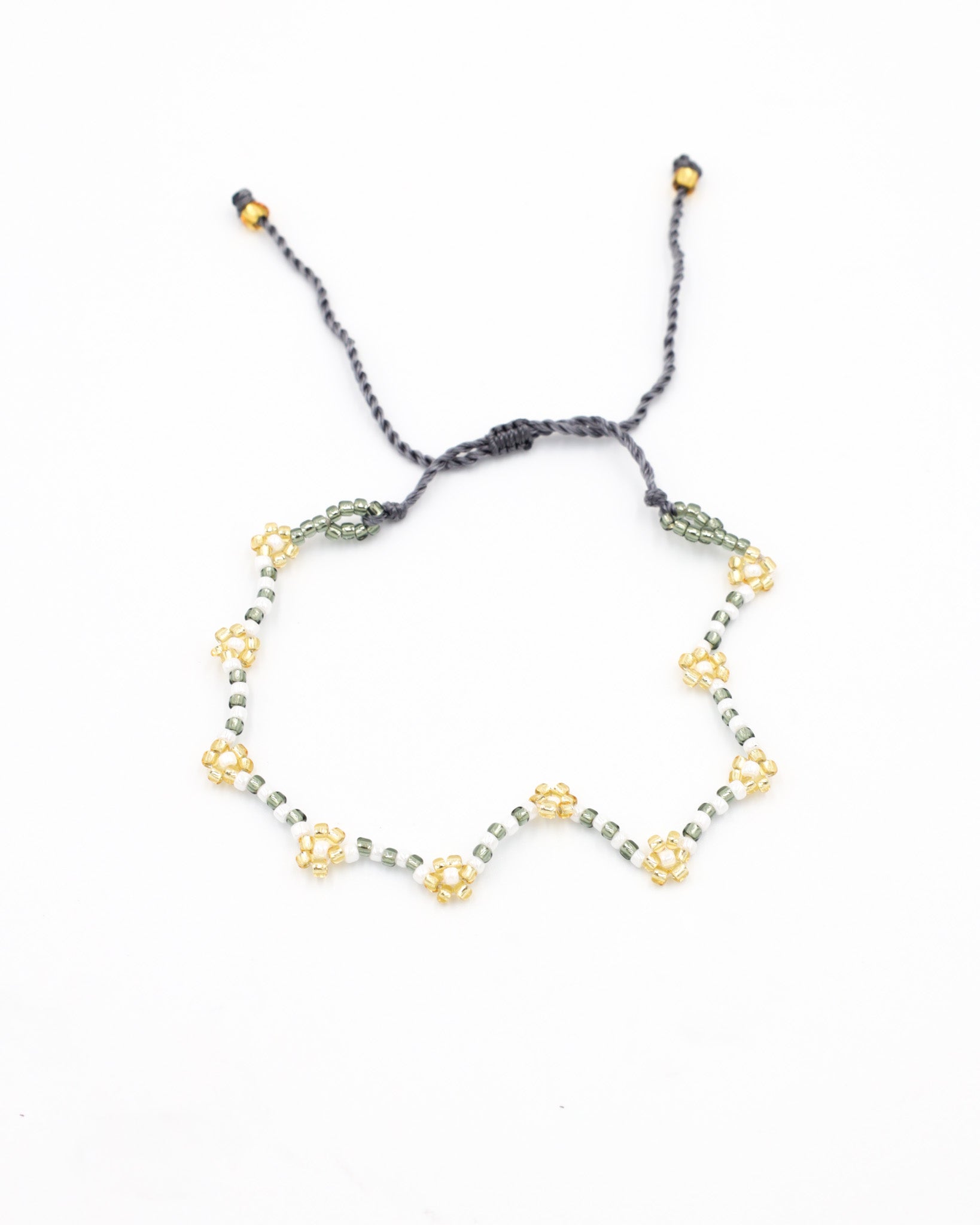 Beaded bracelet in gray, white and gold tones with a zigzag pattern and adjustable sliding closure, laid flat on a white background.