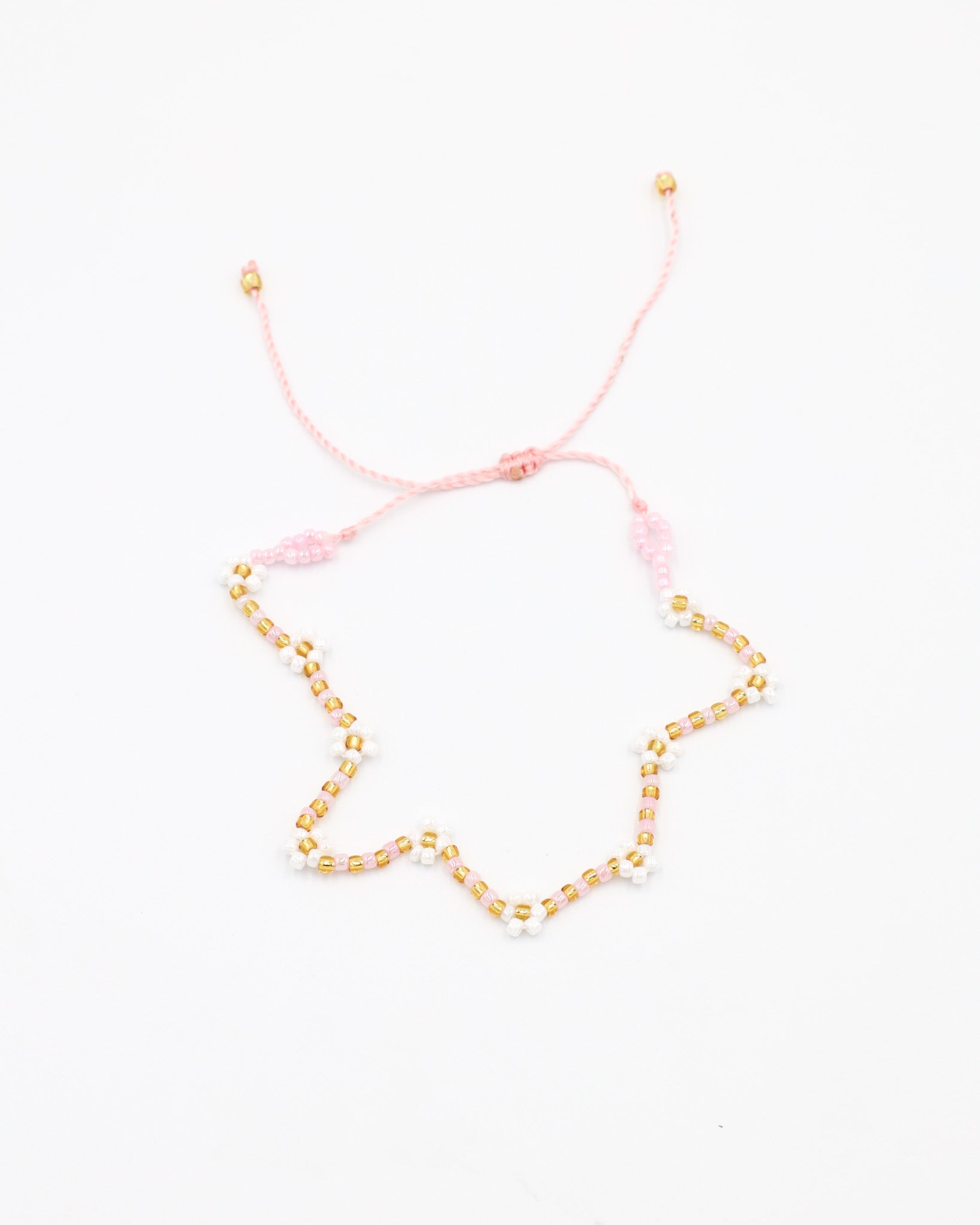 Beaded bracelet in light pink, white and gold tones with a zigzag pattern and adjustable sliding closure, laid flat on a white background.