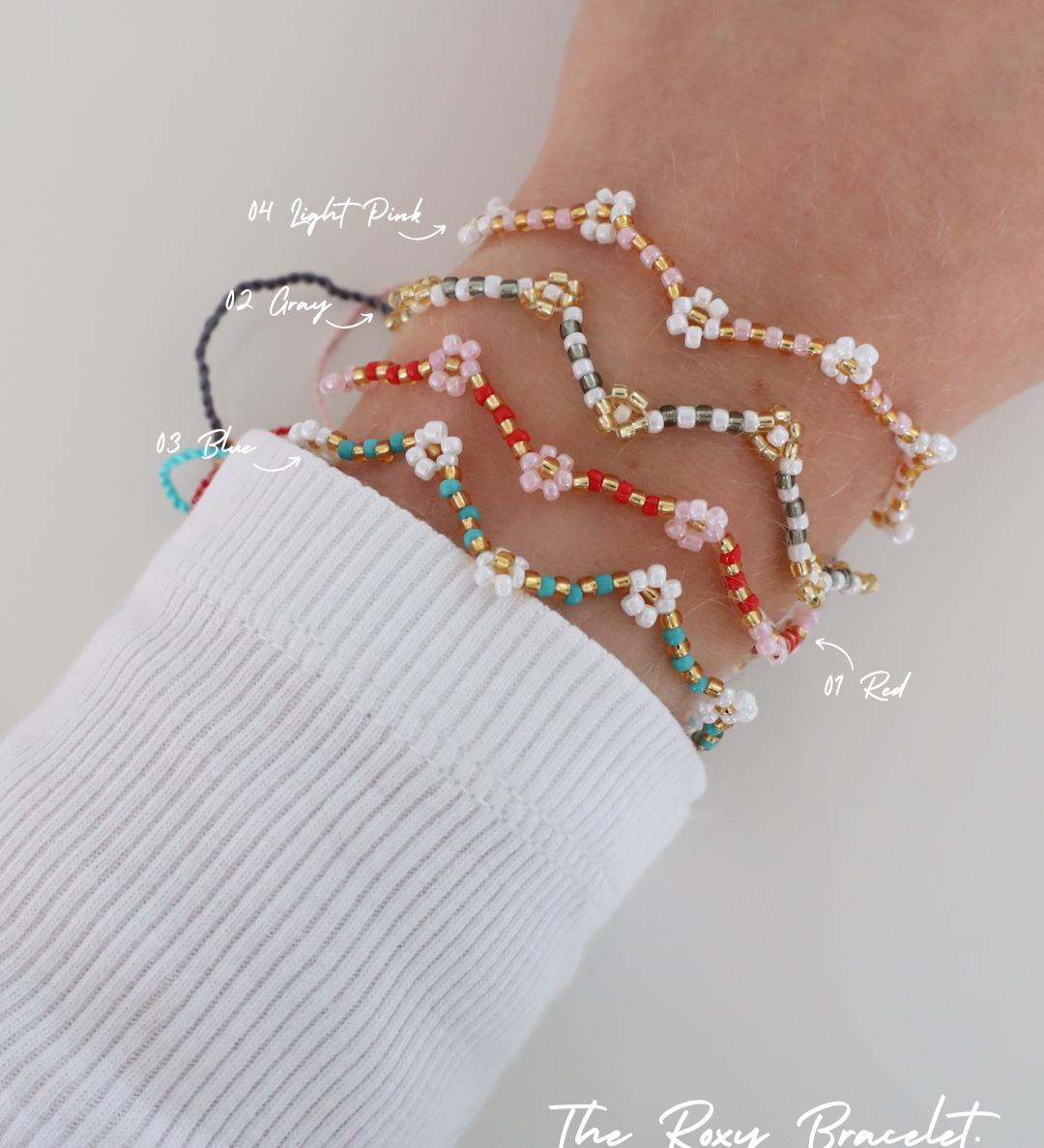 Four Roxy Bracelets in different colors – Red, Blue, Grey, and Light Pink – stacked on a wrist, with each color labeled. The bracelets feature a zigzag beaded pattern with tiny flower details.