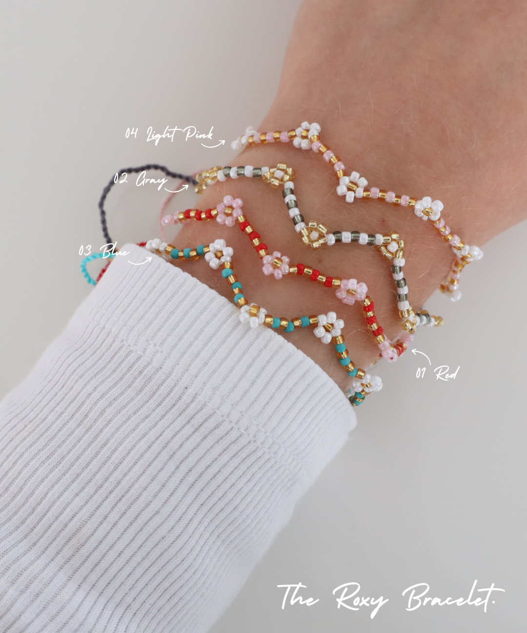 Four Roxy Bracelets in different colors – Red, Blue, Grey, and Light Pink – stacked on a wrist, with each color labeled. The bracelets feature a zigzag beaded pattern with tiny flower details.