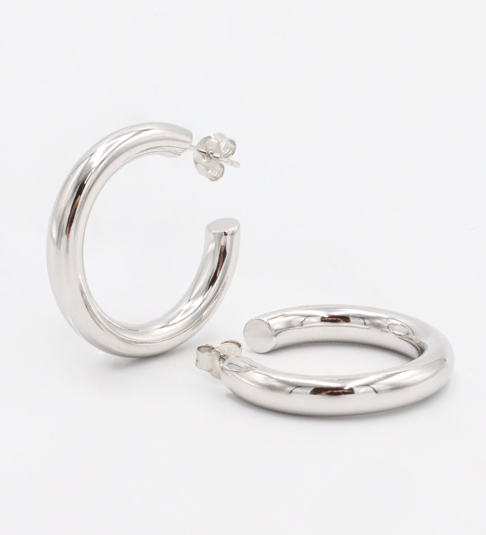 A pair of silver hoop earrings with a visible stud attachment, displayed against a white background.