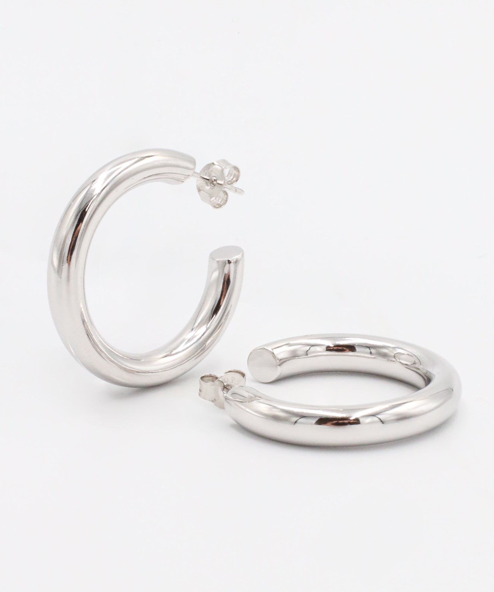 A pair of silver hoop earrings with a visible stud attachment, displayed against a white background.
