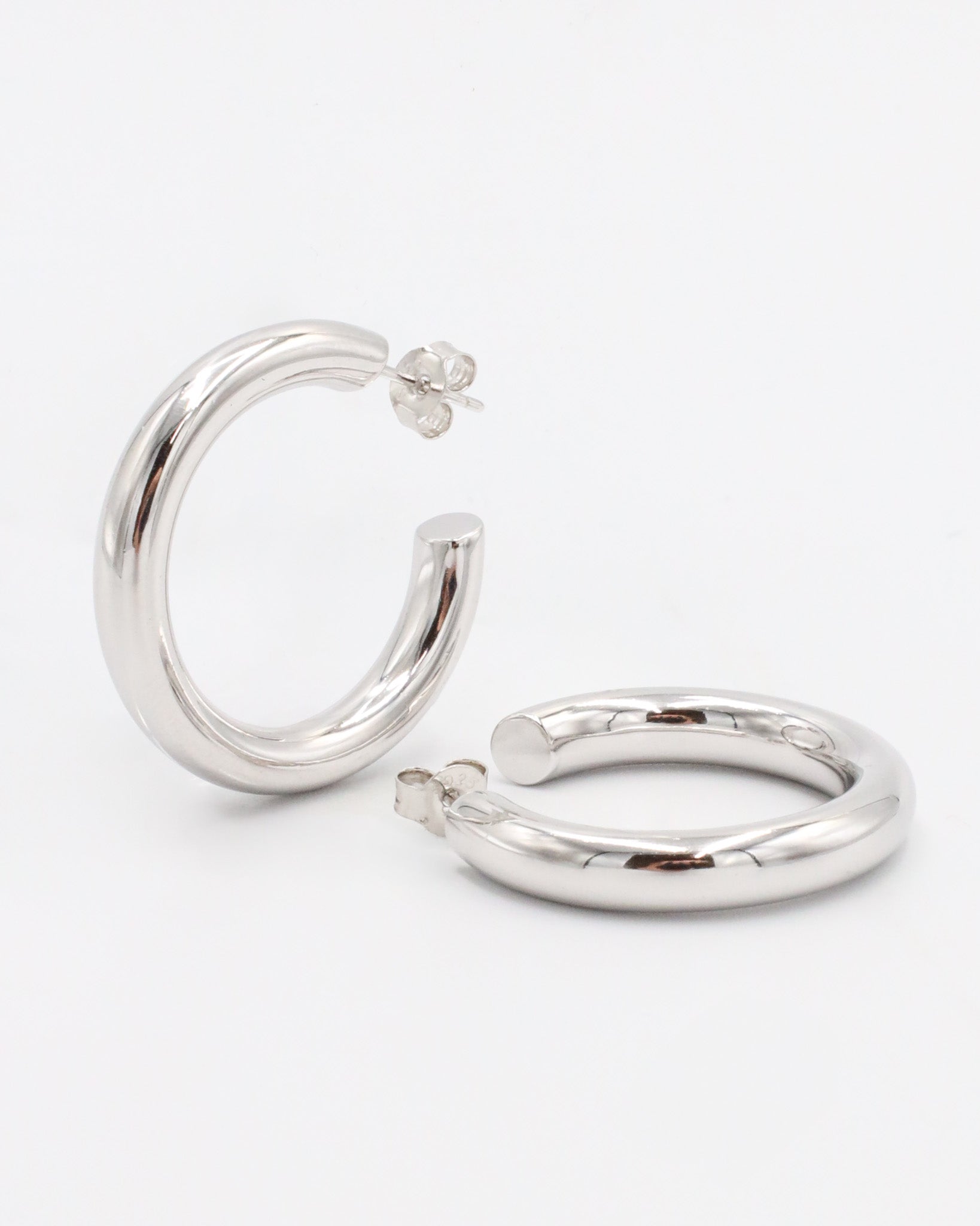 A pair of silver hoop earrings with a visible stud attachment, displayed against a white background.