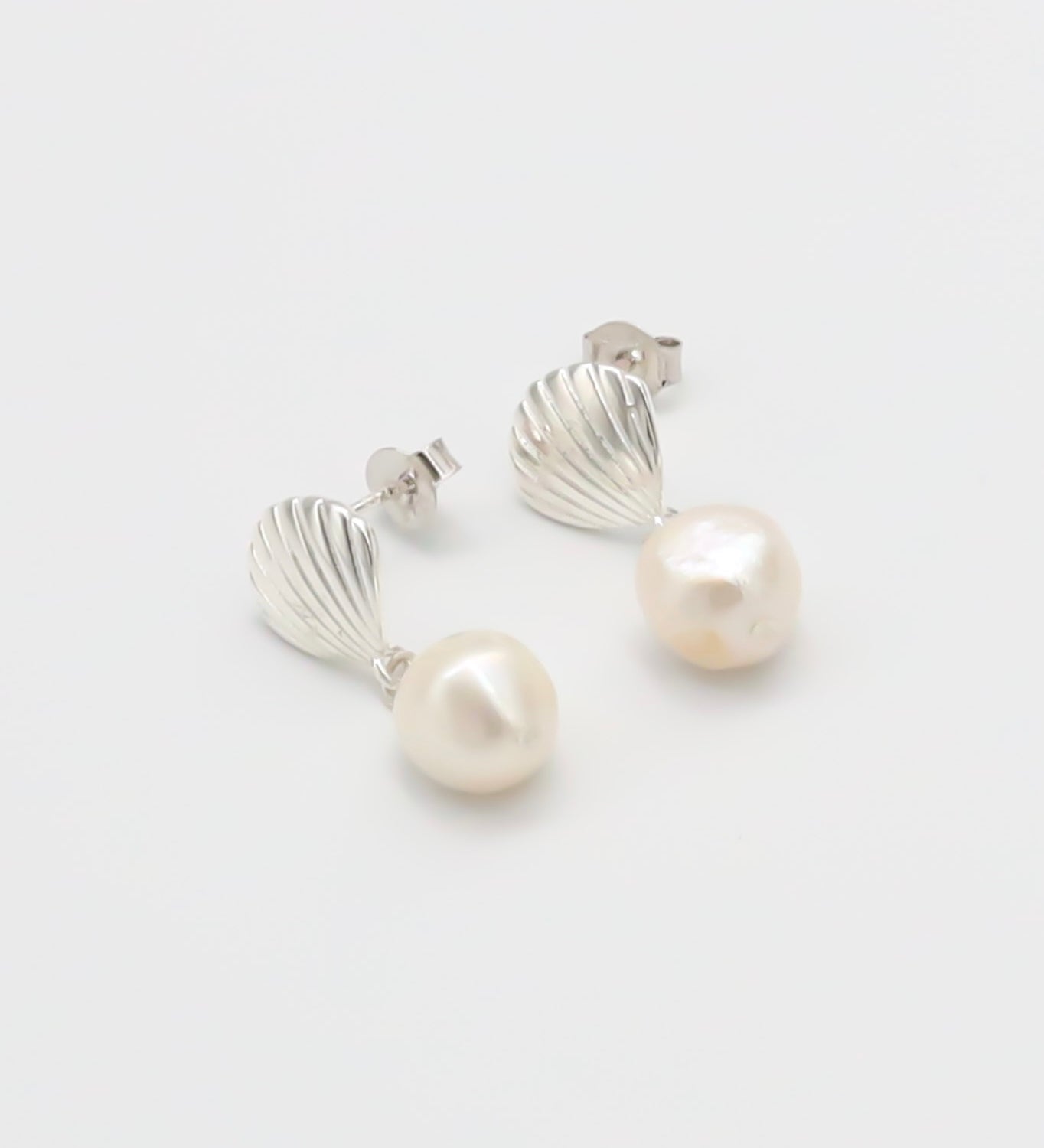 A pair of silver hoop earrings with white pearl accents on a white background.