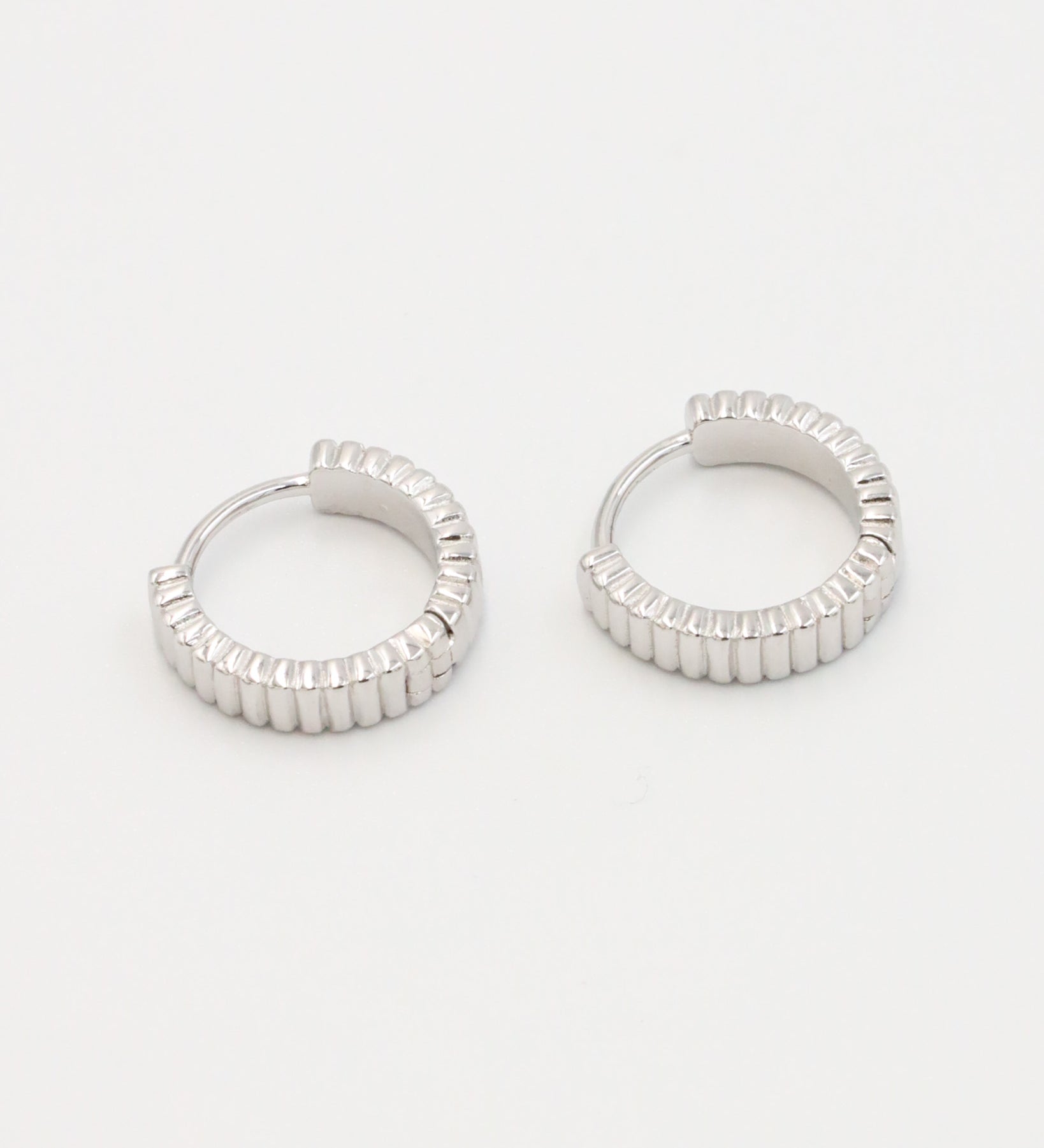 A pair of silver hoop earrings with a textured surface, displayed against a white background.
