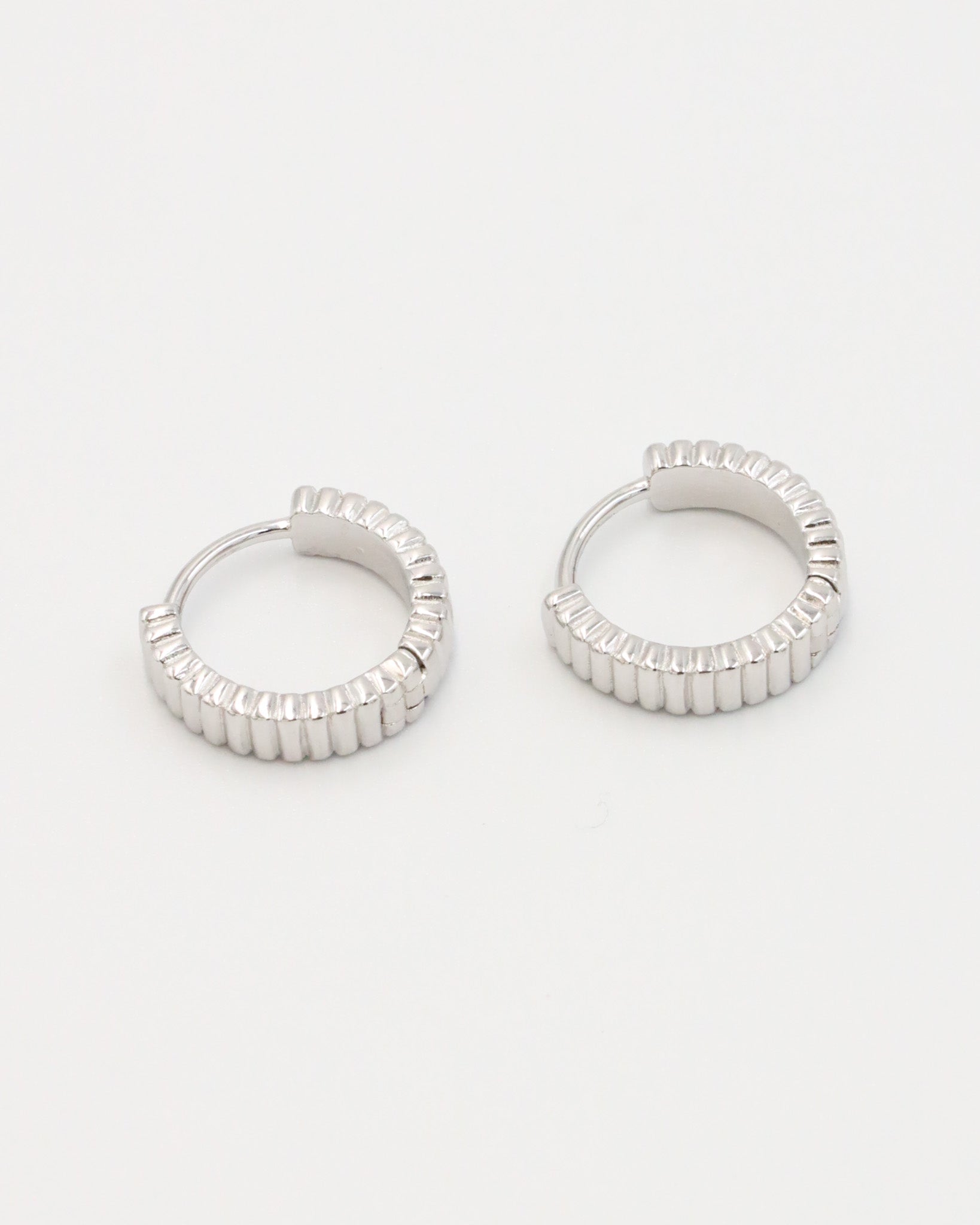 A pair of silver hoop earrings with a textured surface, displayed against a white background.