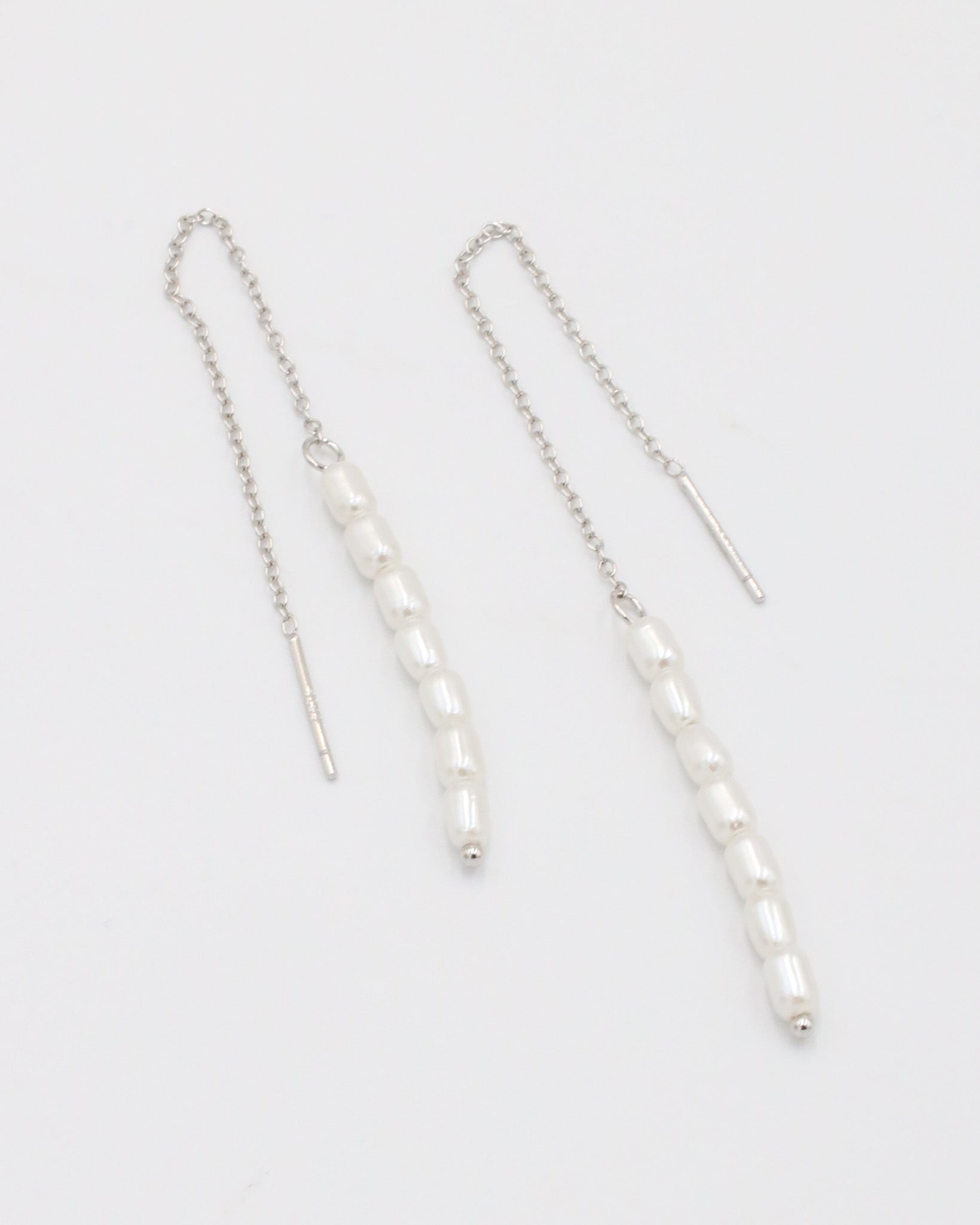 A silver necklace with two white beads on a chain, laid out against a white background.