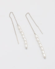A silver necklace with two white beads on a chain, laid out against a white background.