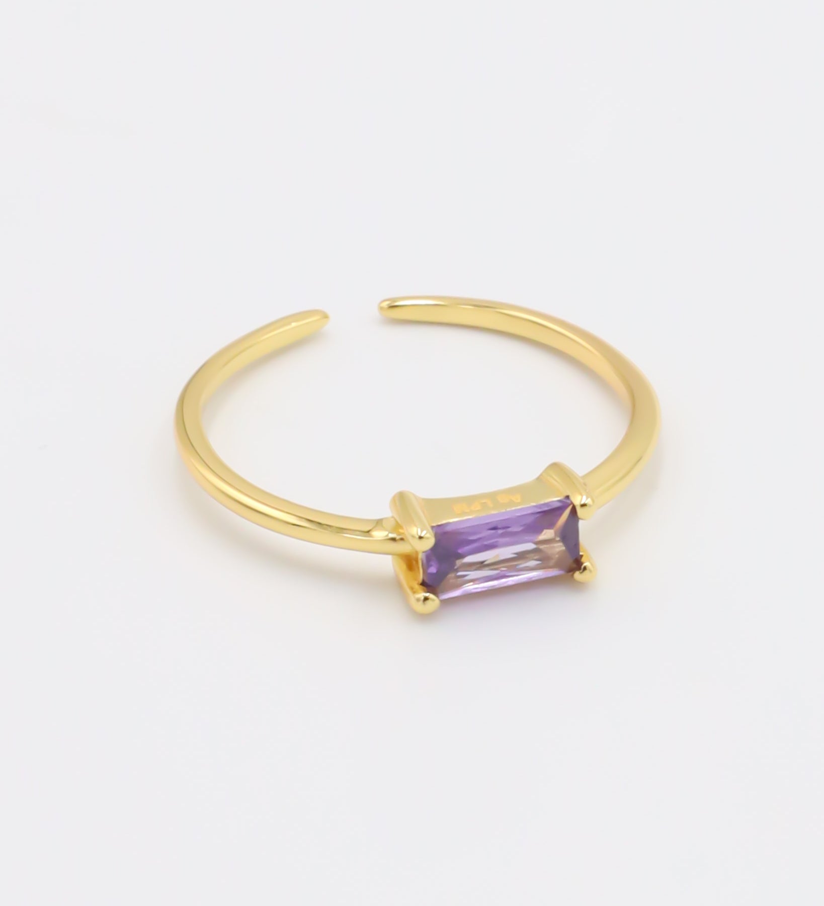 A gold-colored ring with an adjustable band and a rectangular purple gemstone.