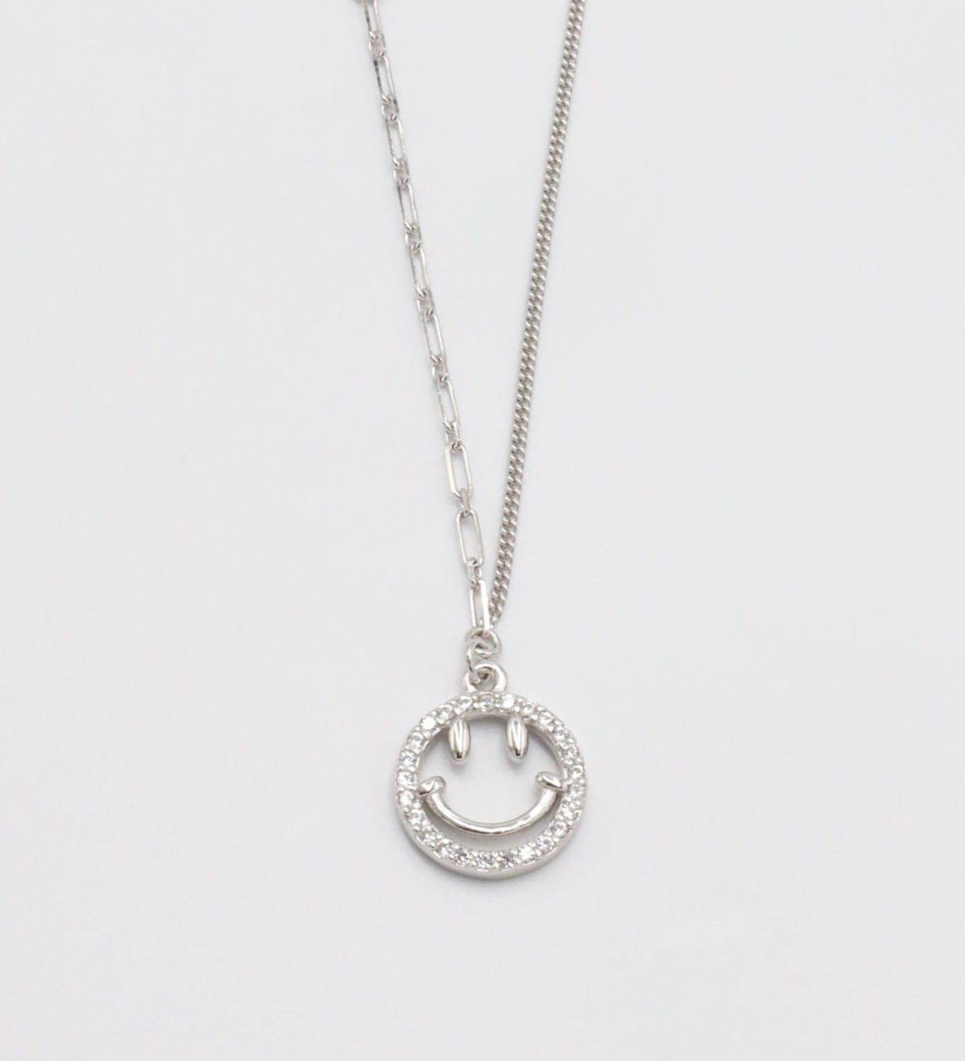 A silver necklace with a circular pendant featuring a smiley face design, displayed against a white background.