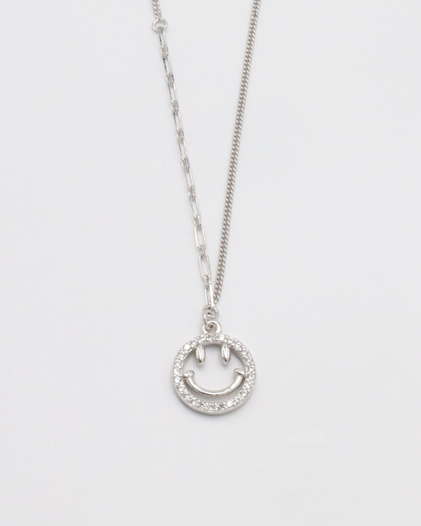A silver necklace with a circular pendant featuring a smiley face design, displayed against a white background.